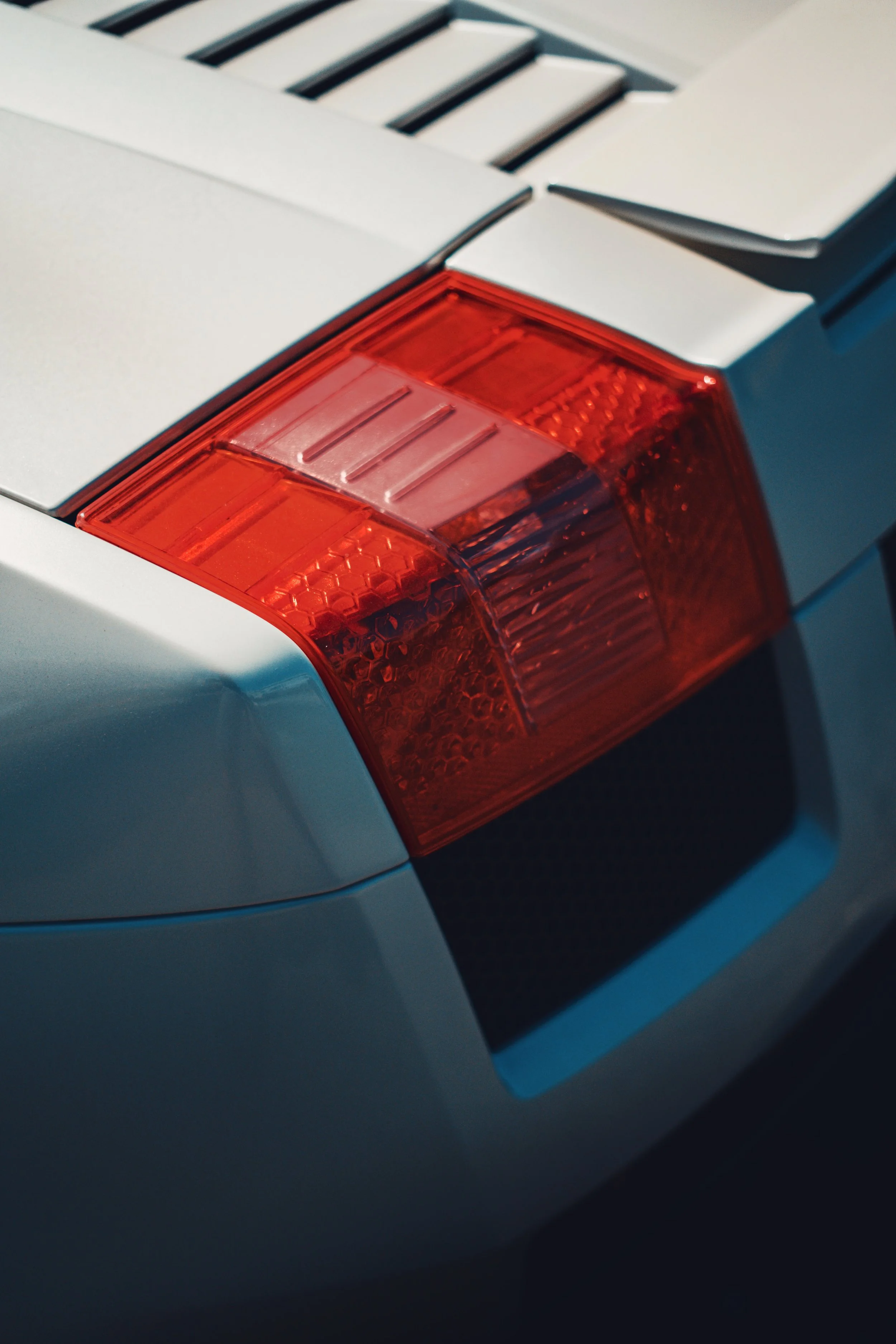 Close-up of a car's taillight and rear panel, with a white body and black vents above the taillight.