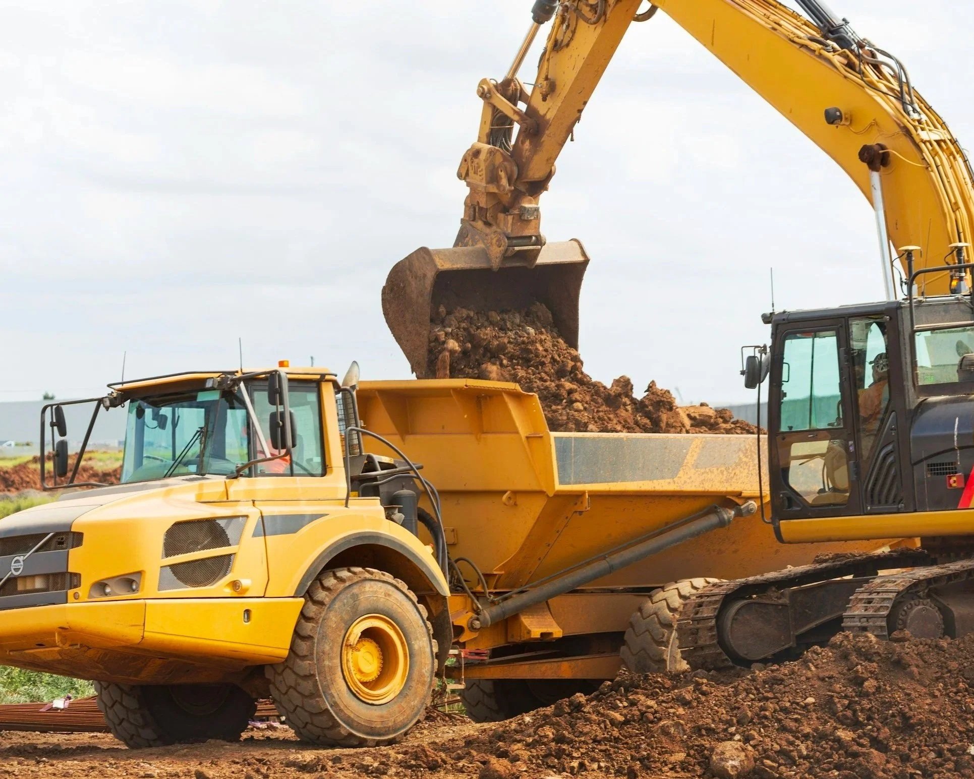 Construction site with yellow and black excavators moving dirt.