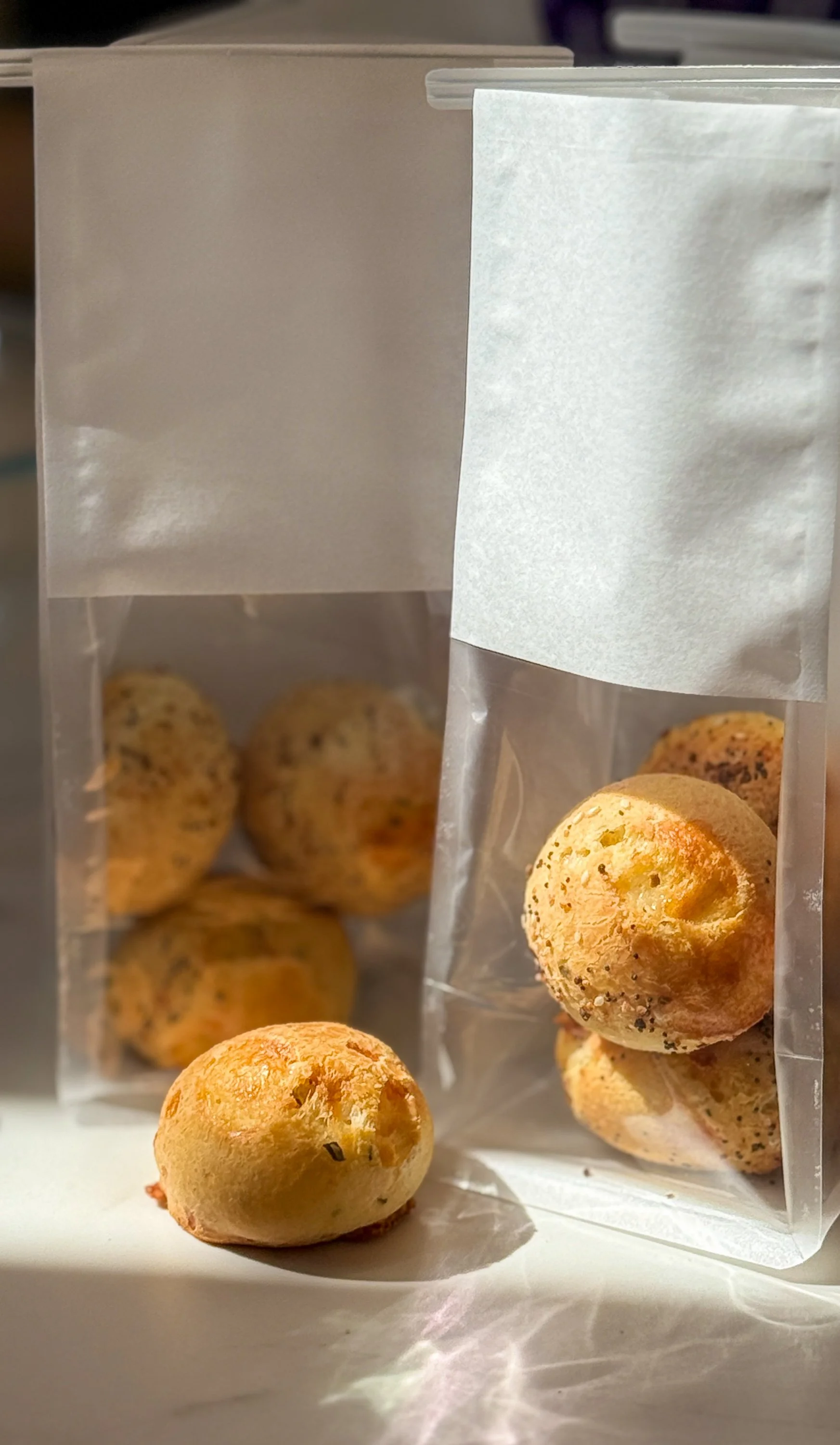 Close-up of a clear plastic bag containing baked goods with seeds, with one baked good placed outside the bag on a white surface.