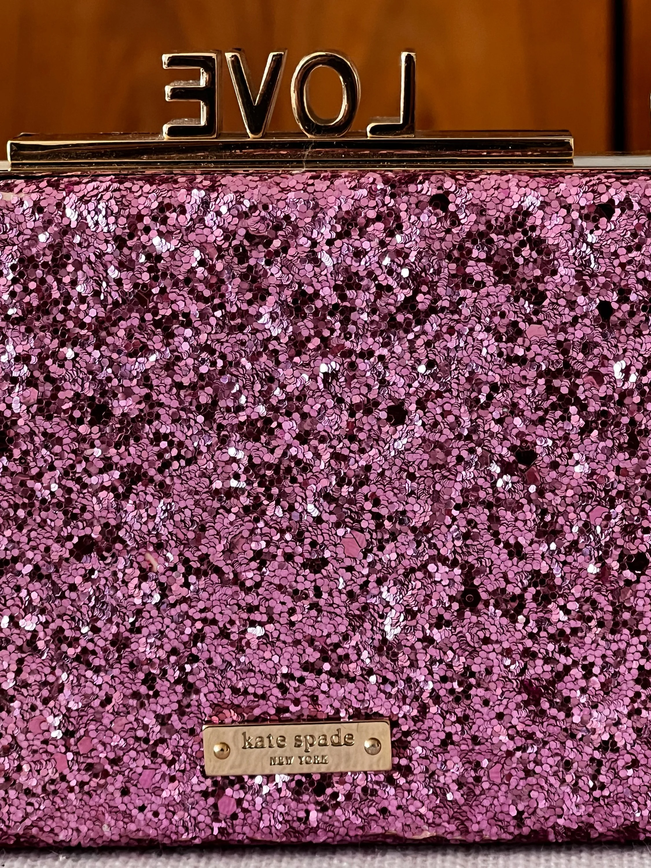 A pink glittery clutch purse with a gold metal plaque that says 'kate spade new york'.