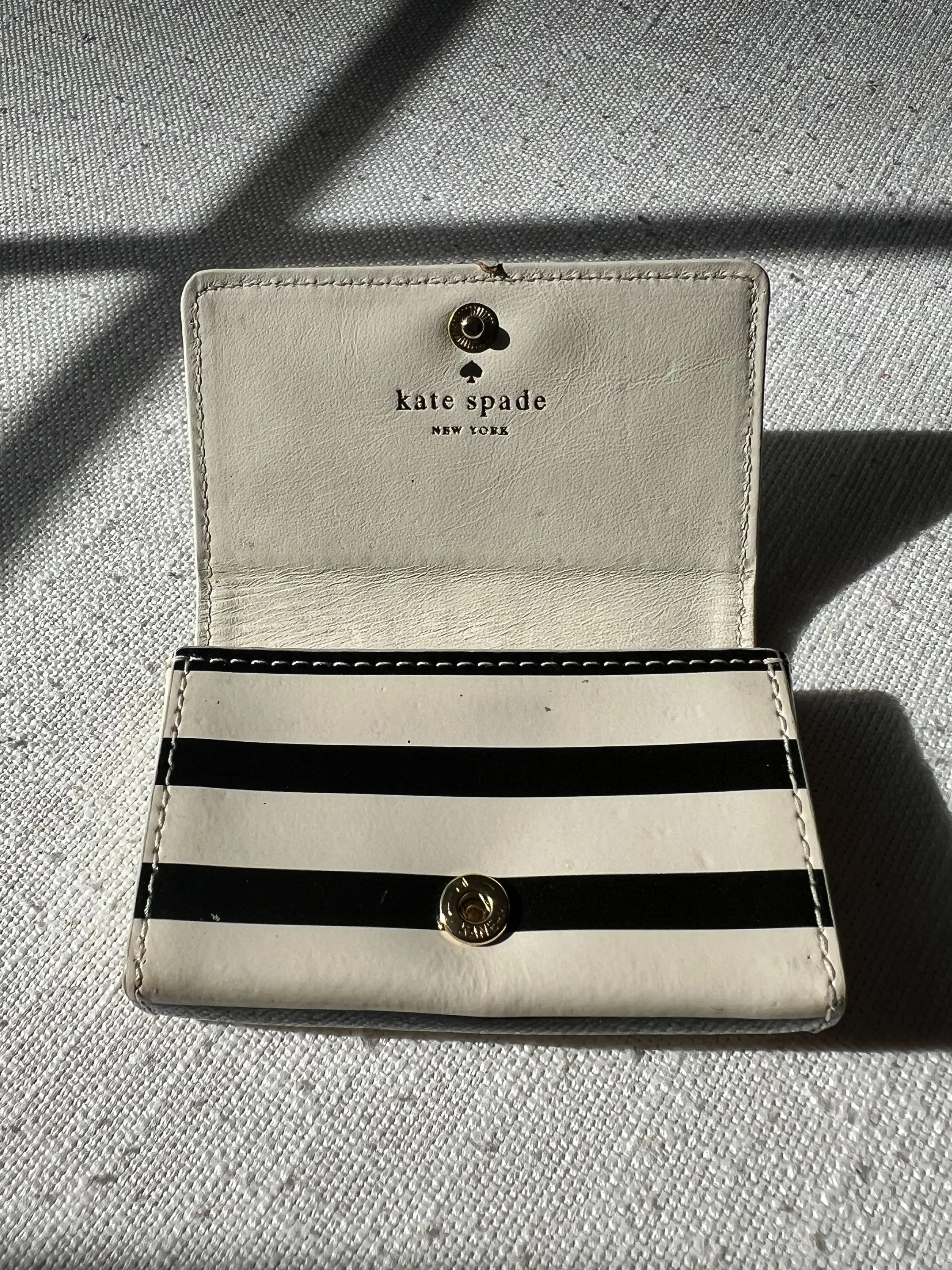 A Kate Spade New York wallet with black and white horizontal stripes, placed on a textured gray fabric surface.