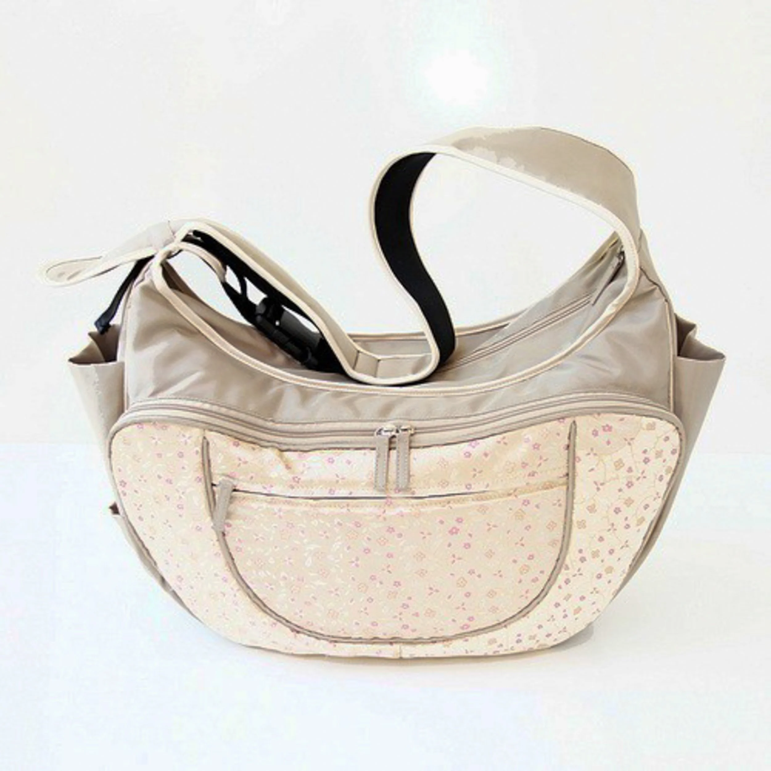A cream-colored diaper bag by Warm Milk Inc.,  with a floral pattern, black handles, and a zipper closure, placed on a white surface.