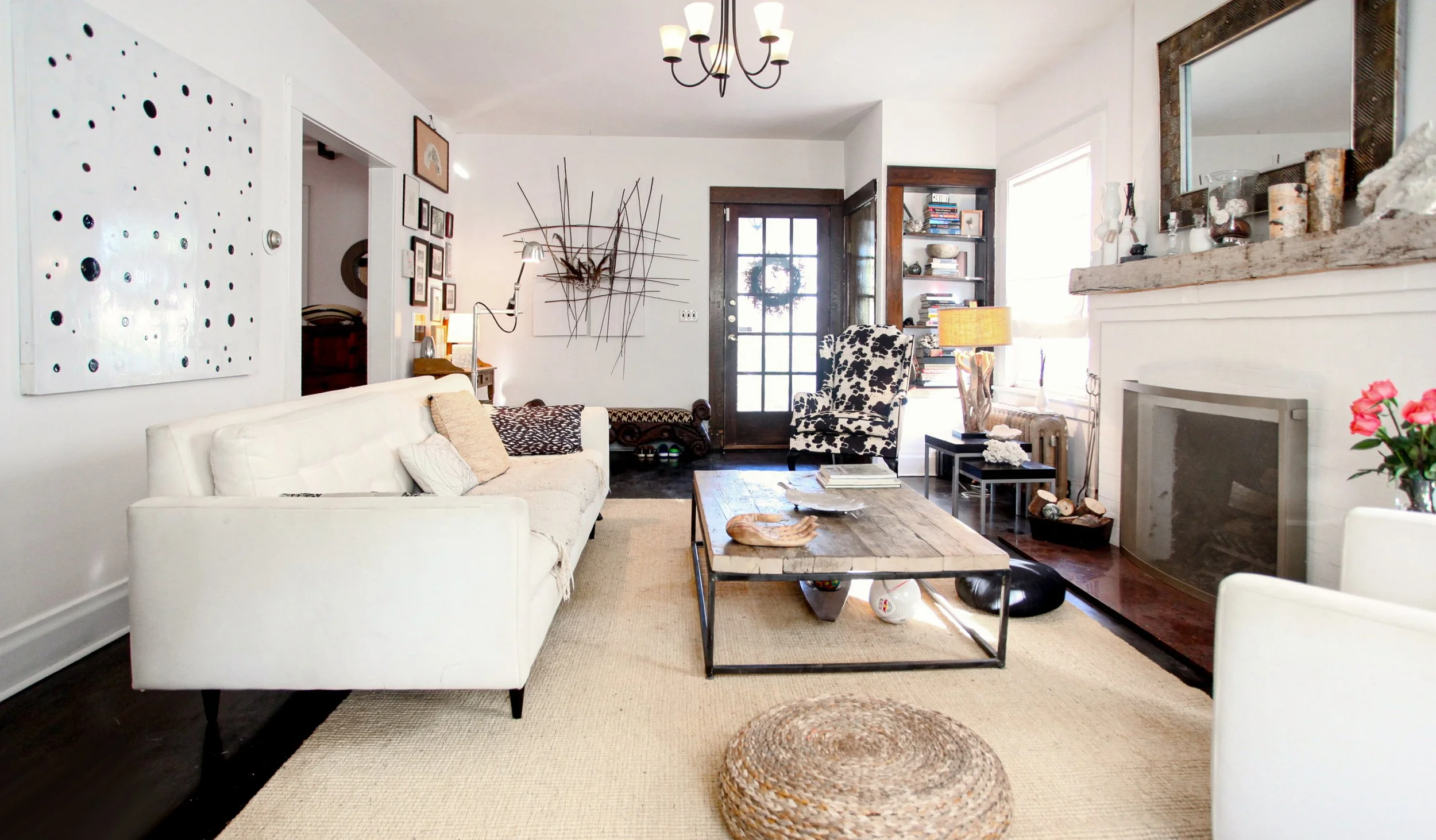Living room with white sofa, cow print armchair, wooden coffee table, wall art, bookshelf, fireplace, and decor.