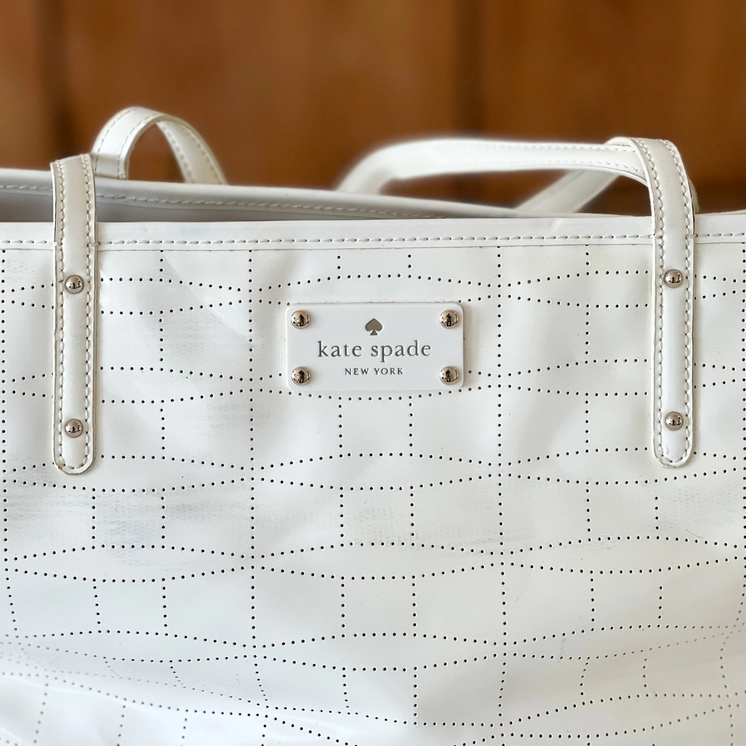 A white handbag with a dotted pattern and metal studs, with a Kate Spade New York label visible on the front.