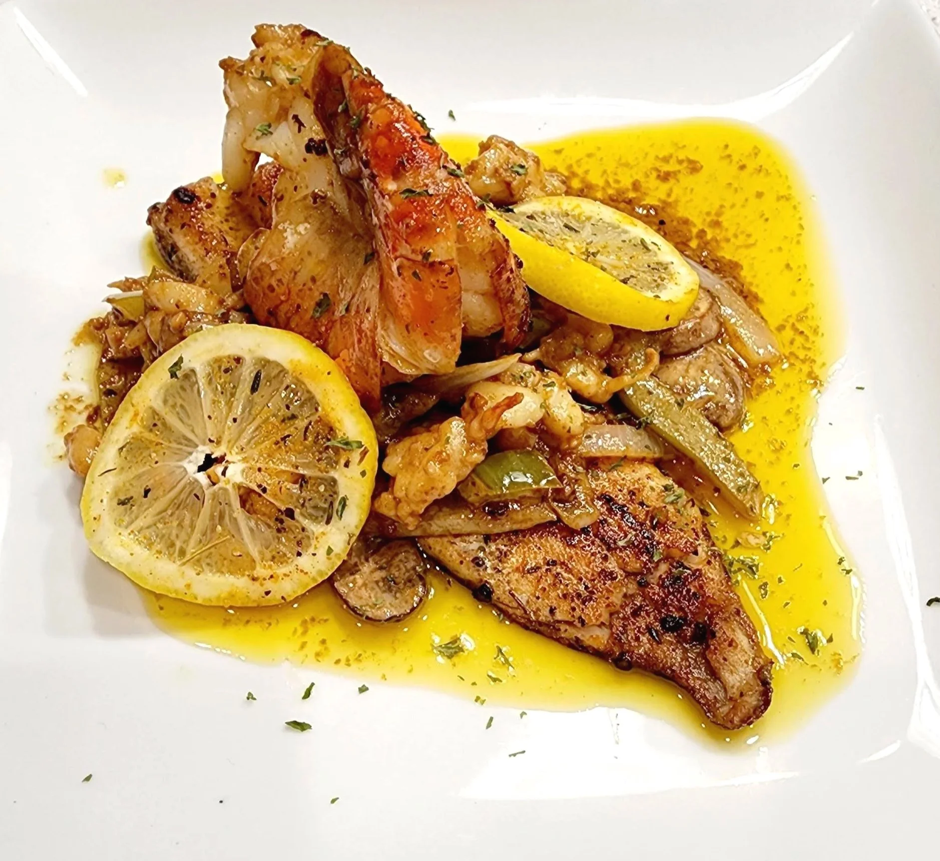 Pan-fried fish fillet served with lemon slices, cooked vegetables, and a drizzle of lemon butter sauce on a white plate.