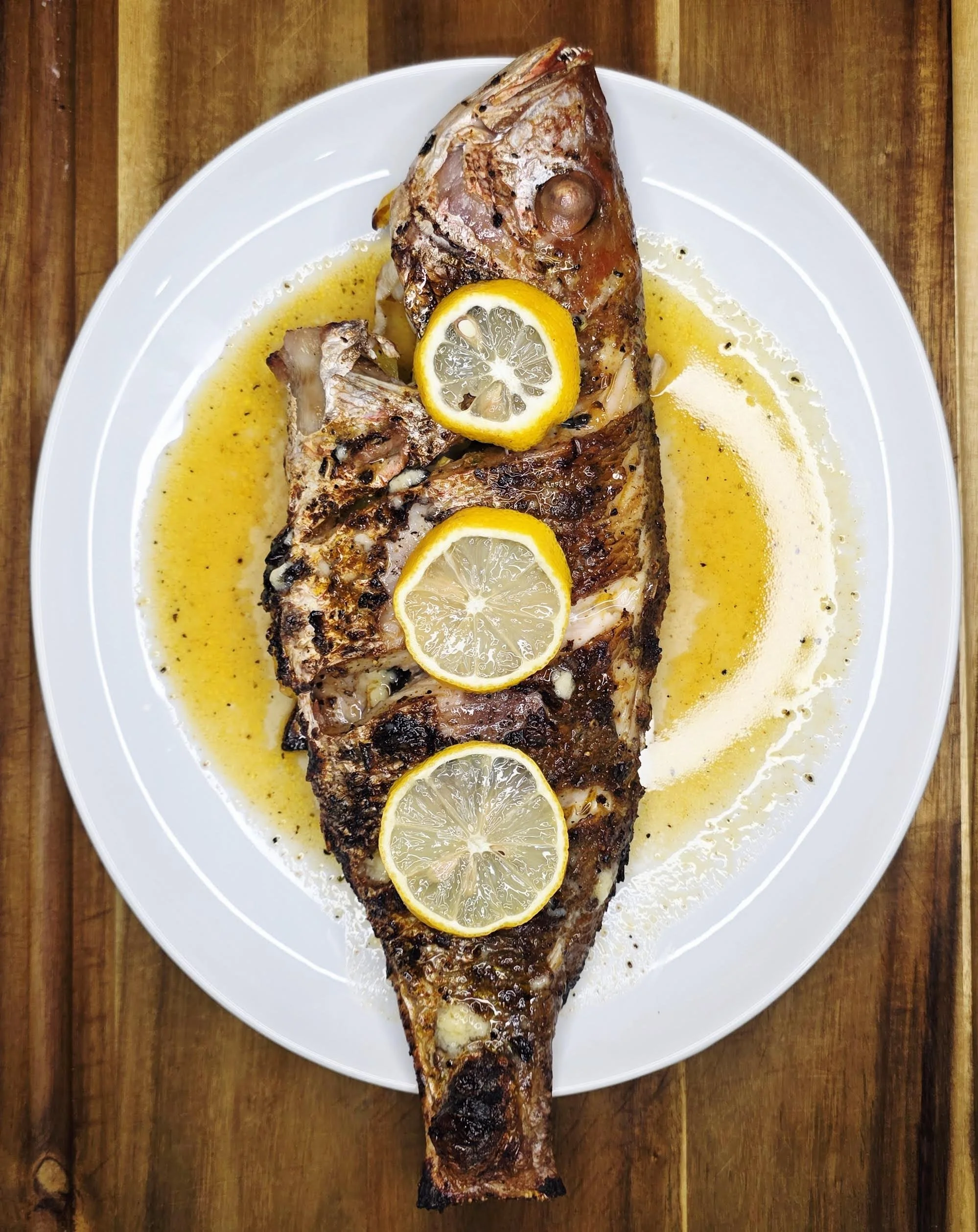 Grilled whole fish topped with lemon slices, served on a white plate with a lemon-butter sauce.