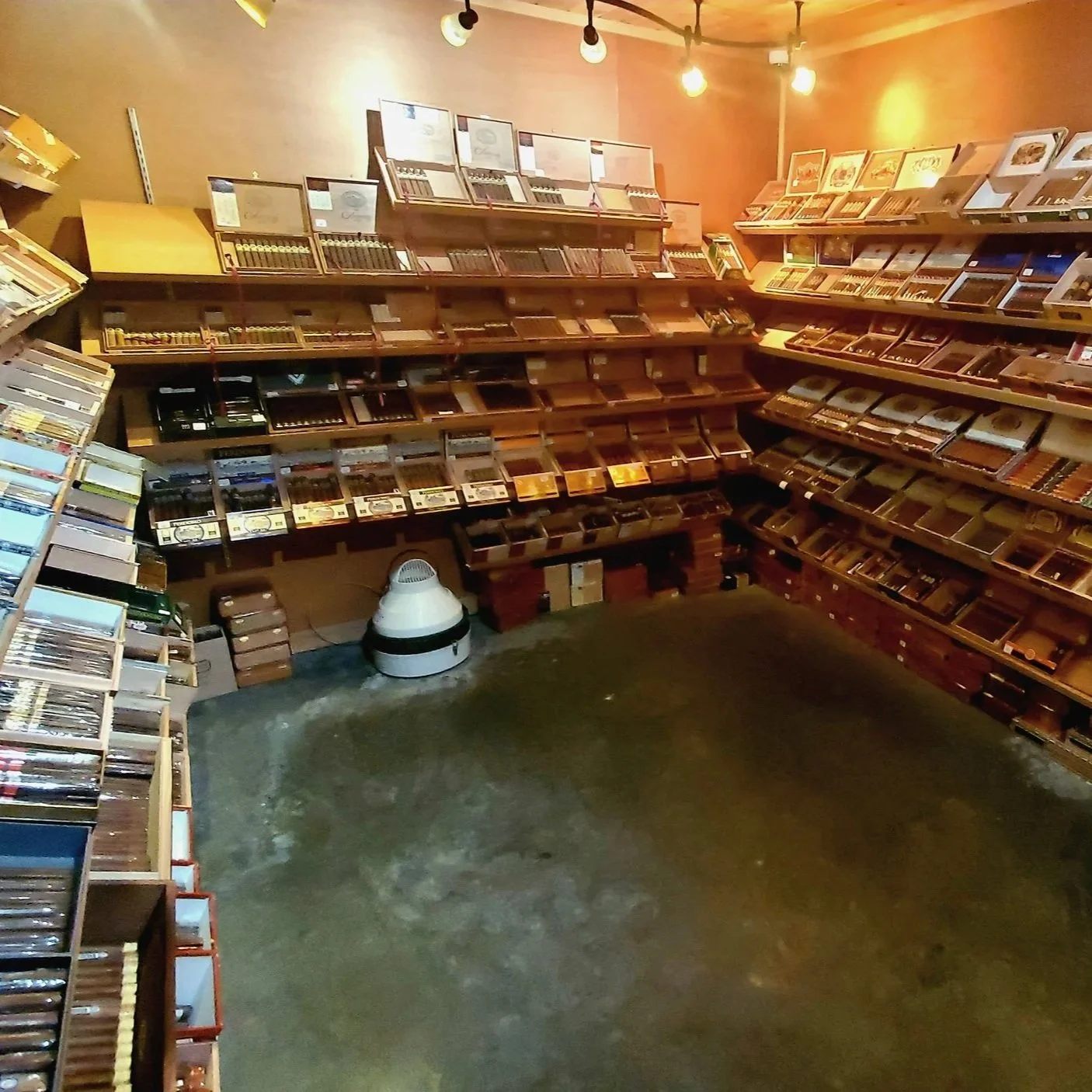 Interior of a cigar shop with wooden shelves filled with cigar boxes and humidifiers, dim lighting, and a concrete floor.