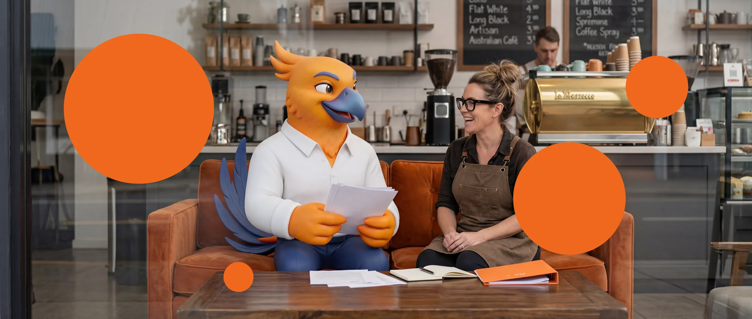 Figurs' Figgy the phoenix mascot sitting on a sofa and holding papers, talking to a woman in glasses and an apron inside a coffee shop.