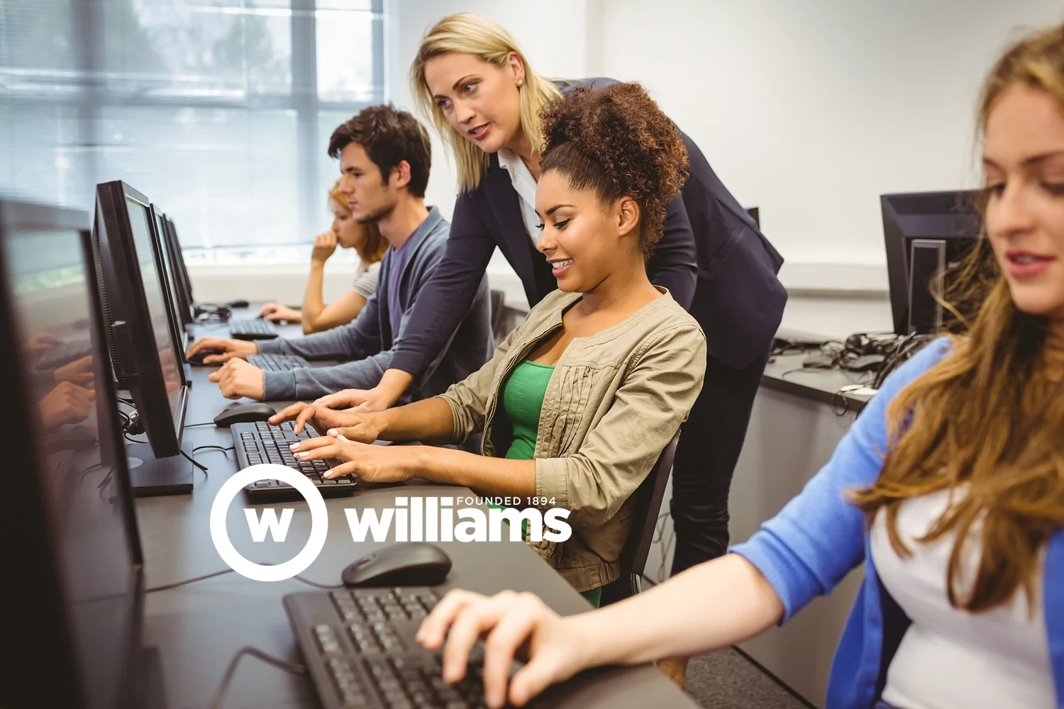 A woman instructor helps female students working on computers in a classroom or computer lab at Williams Business College.