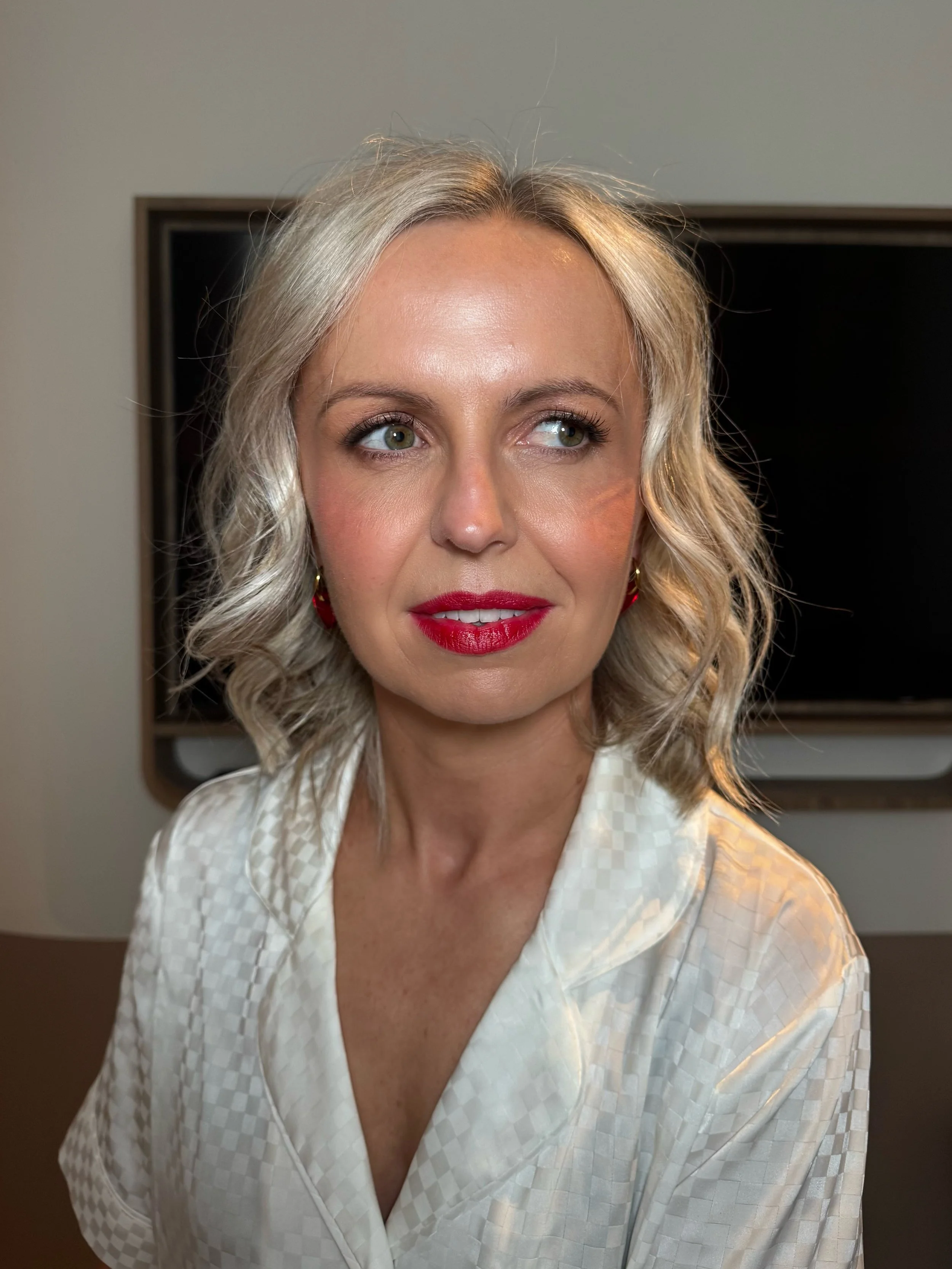 A bride wearing a white robe and red lipstick on her wedding day in a hotel room in Melbourne.