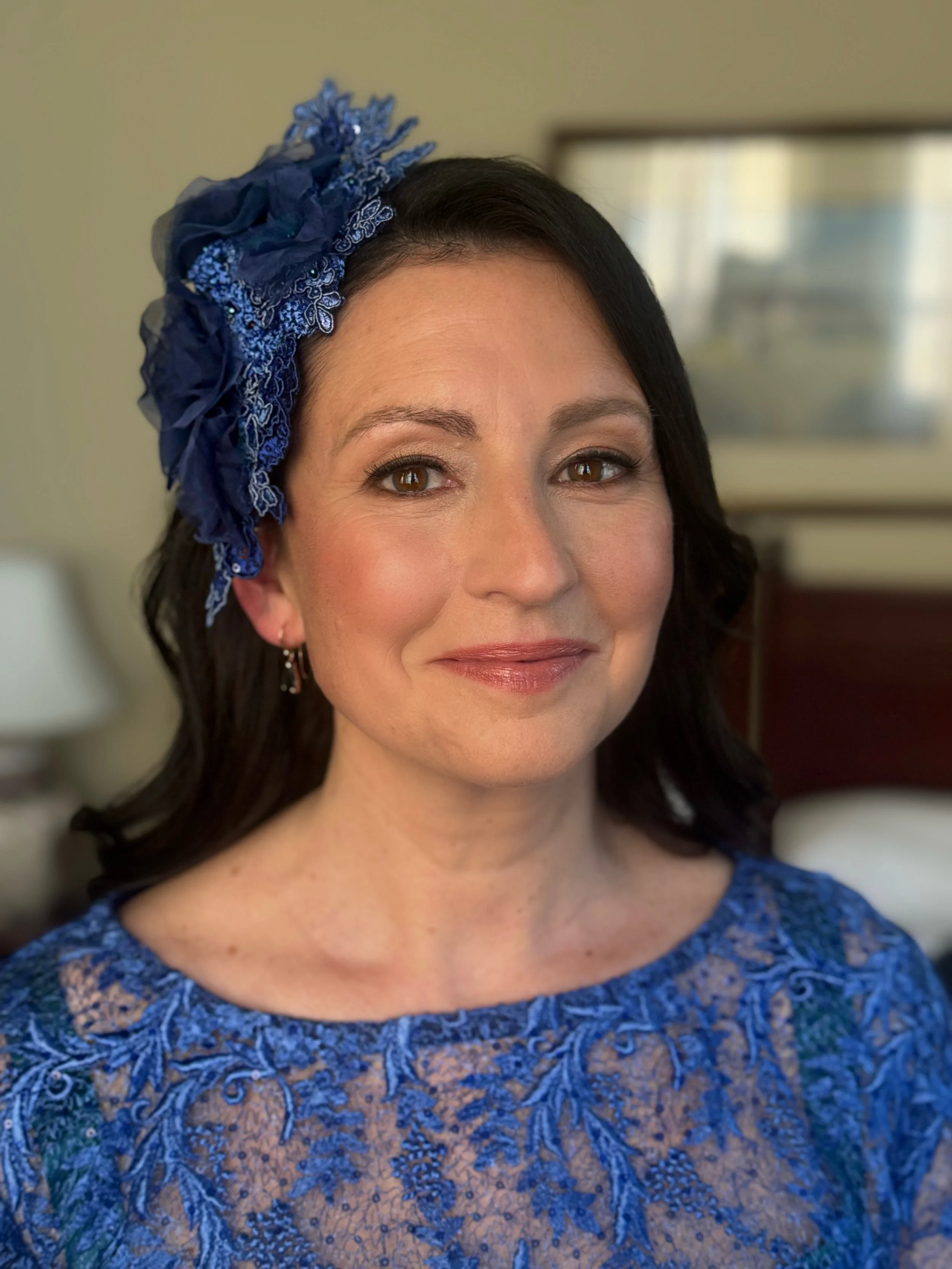 A mature bride wearing a blue wedding dress and co-ordinating headpiece. She is smiling and is being photographed at the Hotel Windsor in Melbourne. Her makeup is emphasising her eyes and her skin is radiant.