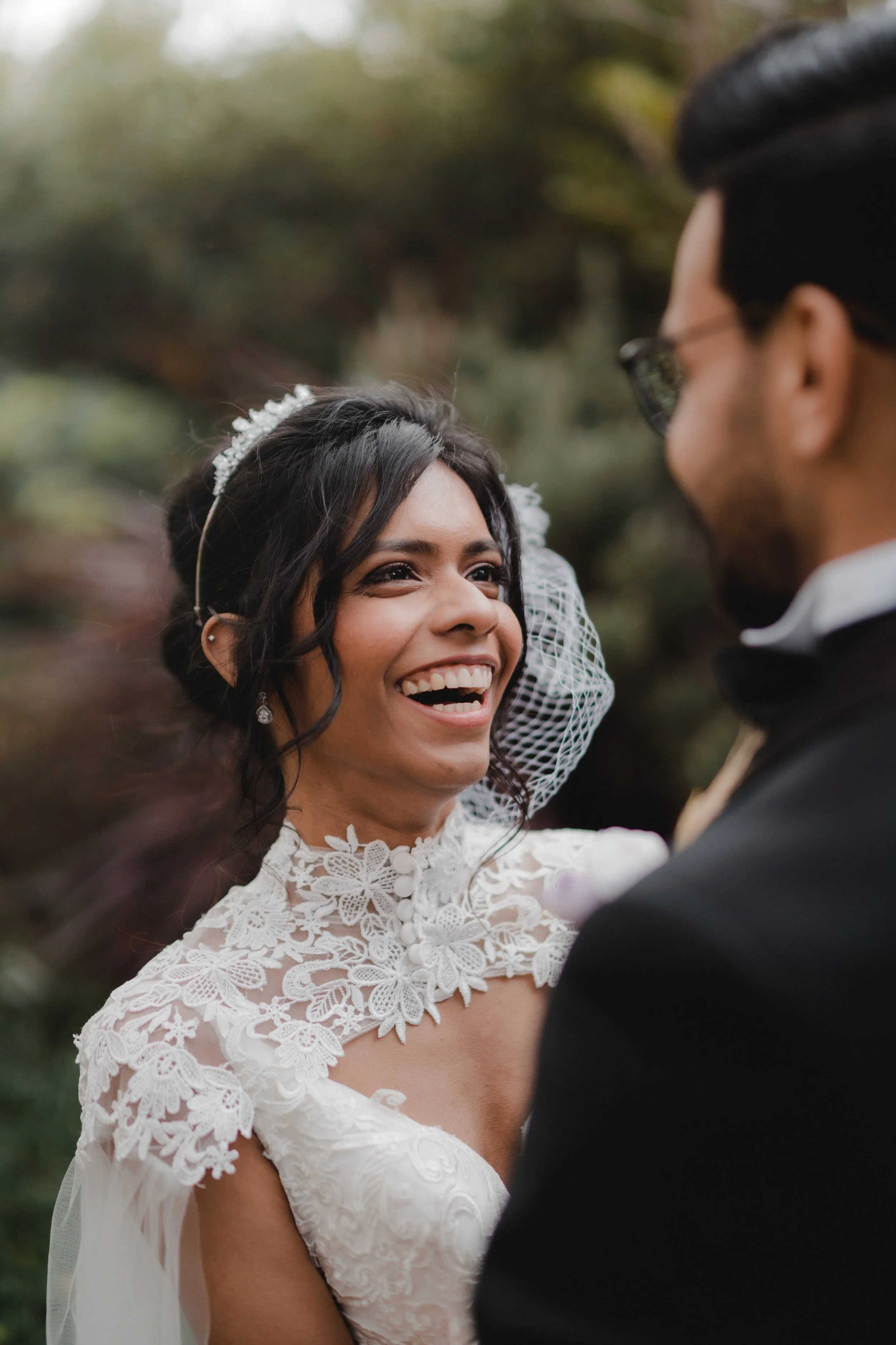 A bride and groom smiling at each other outdoors during their wedding ceremony.