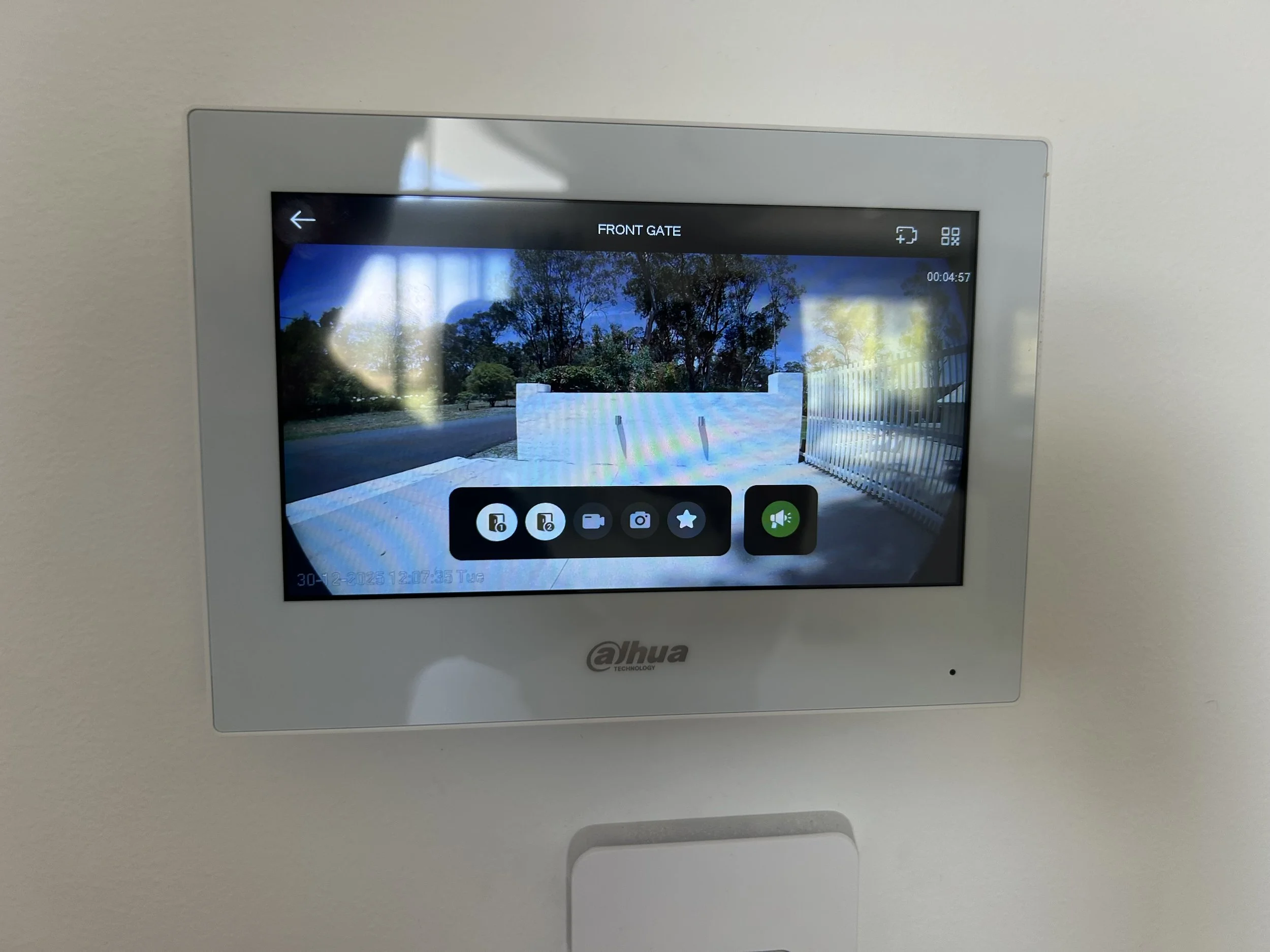 Security control panel displaying a camera view of an outdoor area with trees, a fence, and a clear sky.
