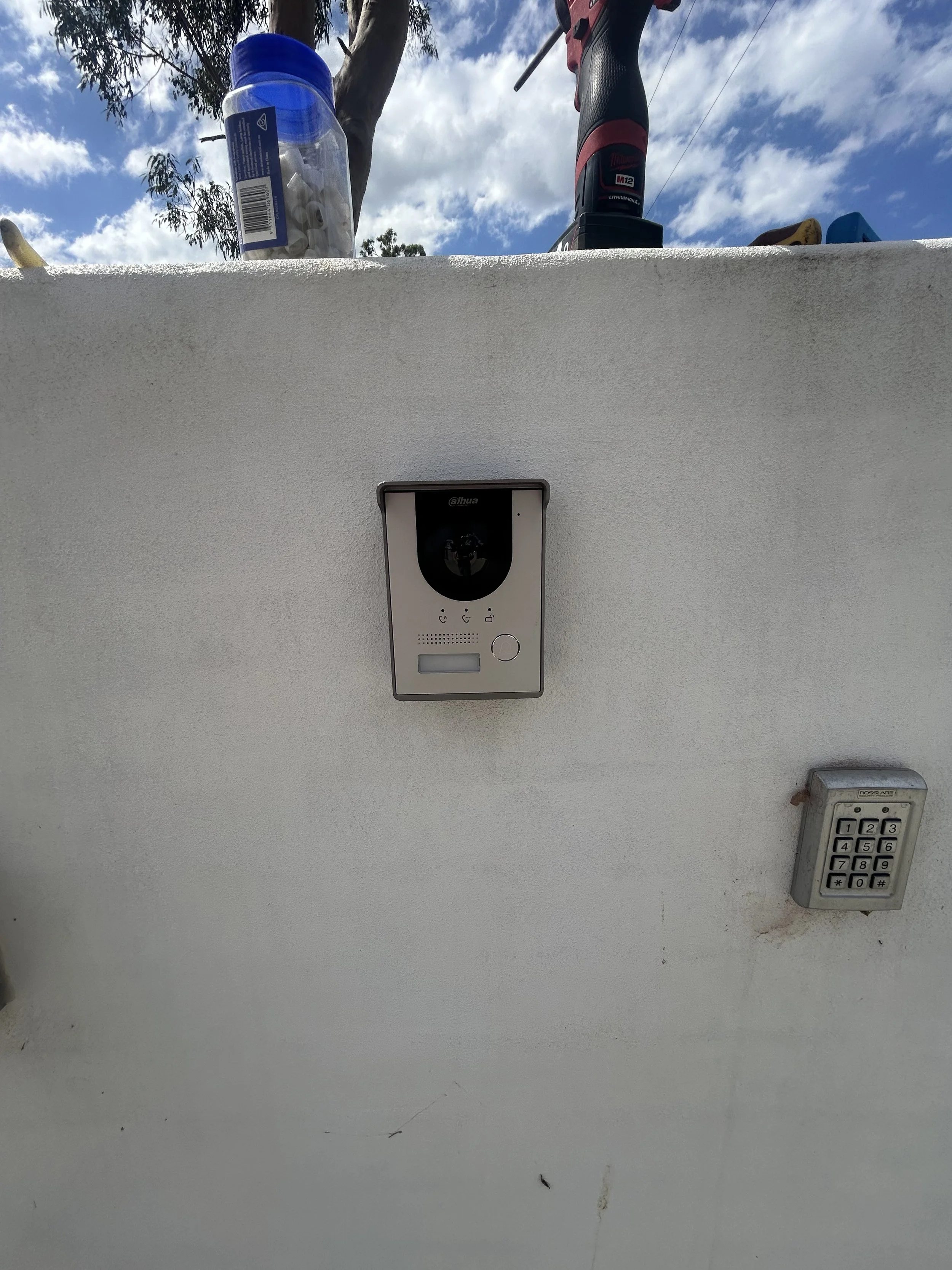 Security camera mounted on a white wall with a keypad and an outdoor sky in the background.