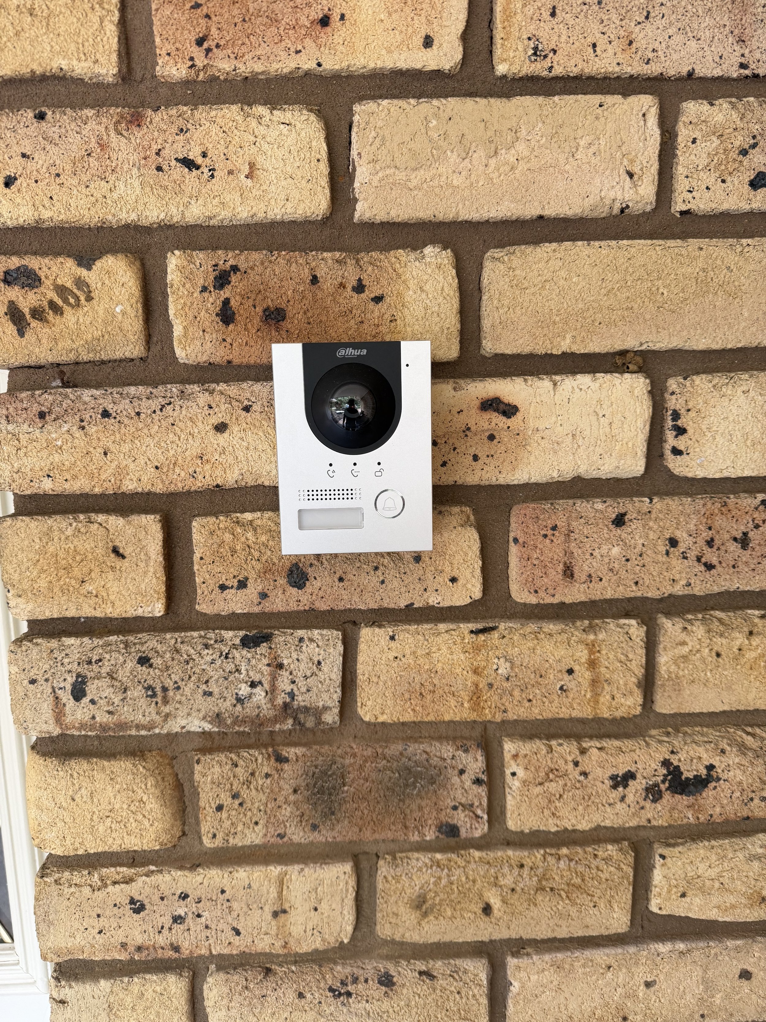 A white video doorbell mounted on a brick wall.
