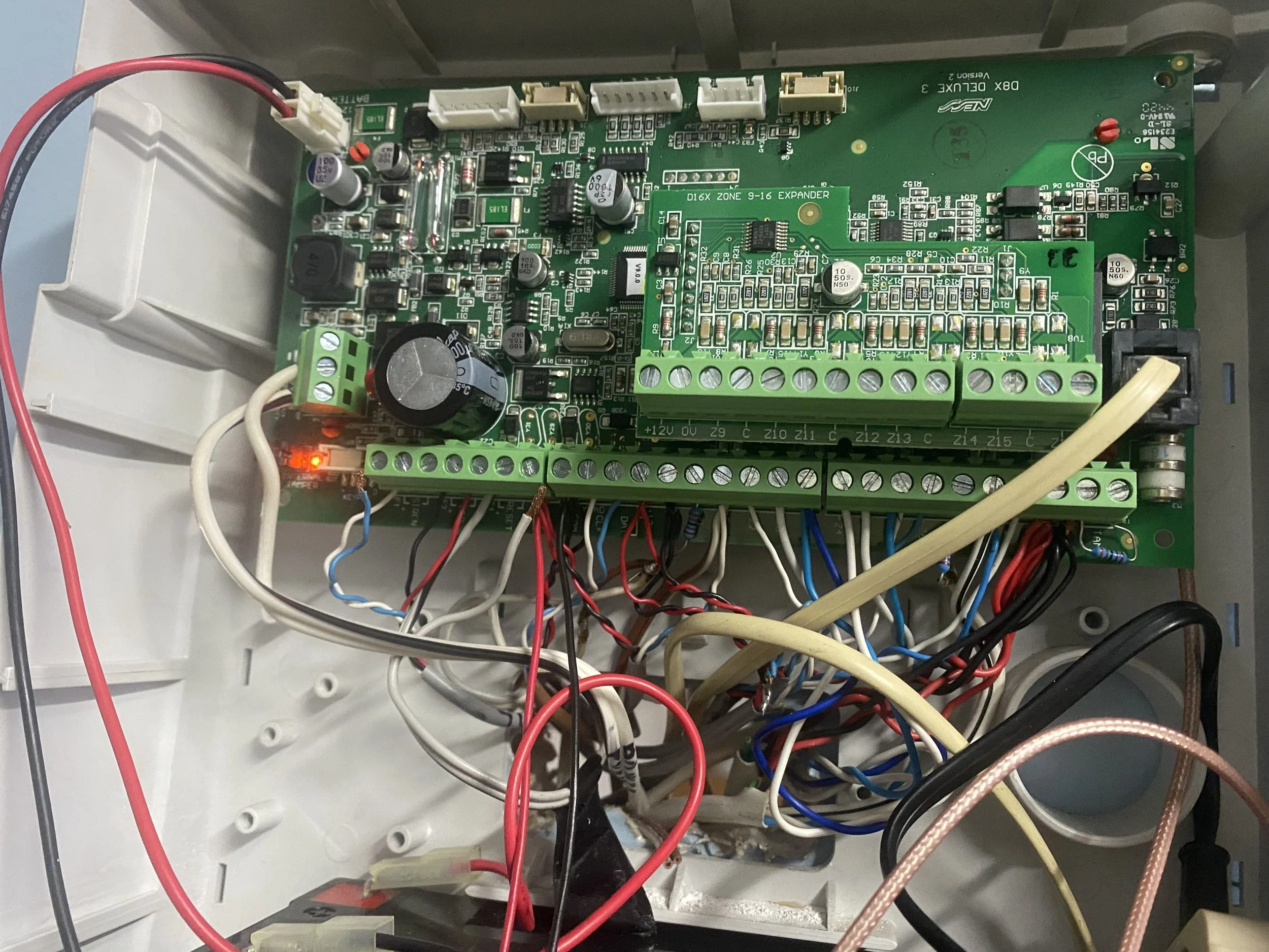 A green circuit board with various electronic components, wires, and connectors inside a white plastic enclosure.