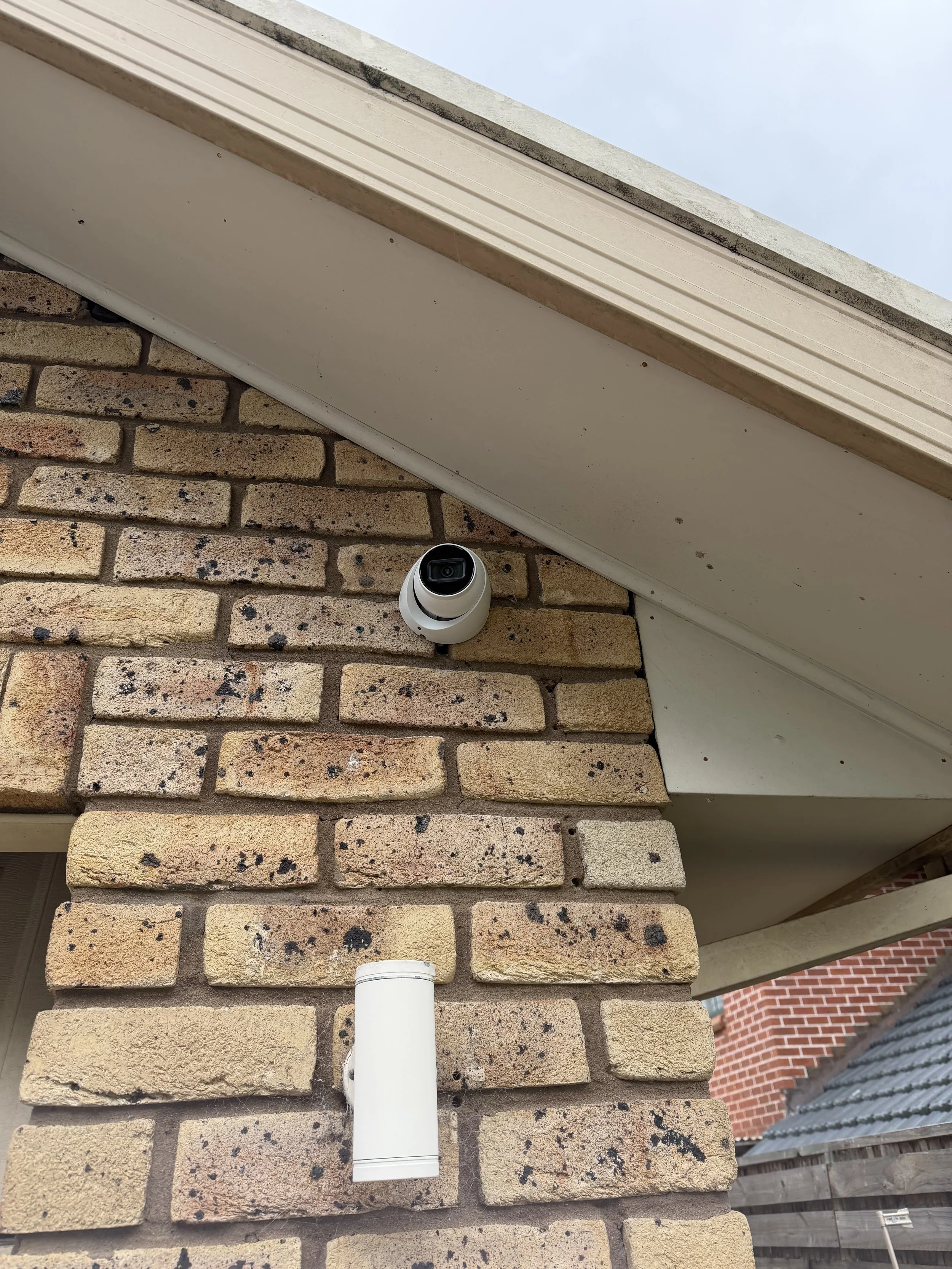 Close-up view of a brick wall with a white security camera mounted under a white soffit.
