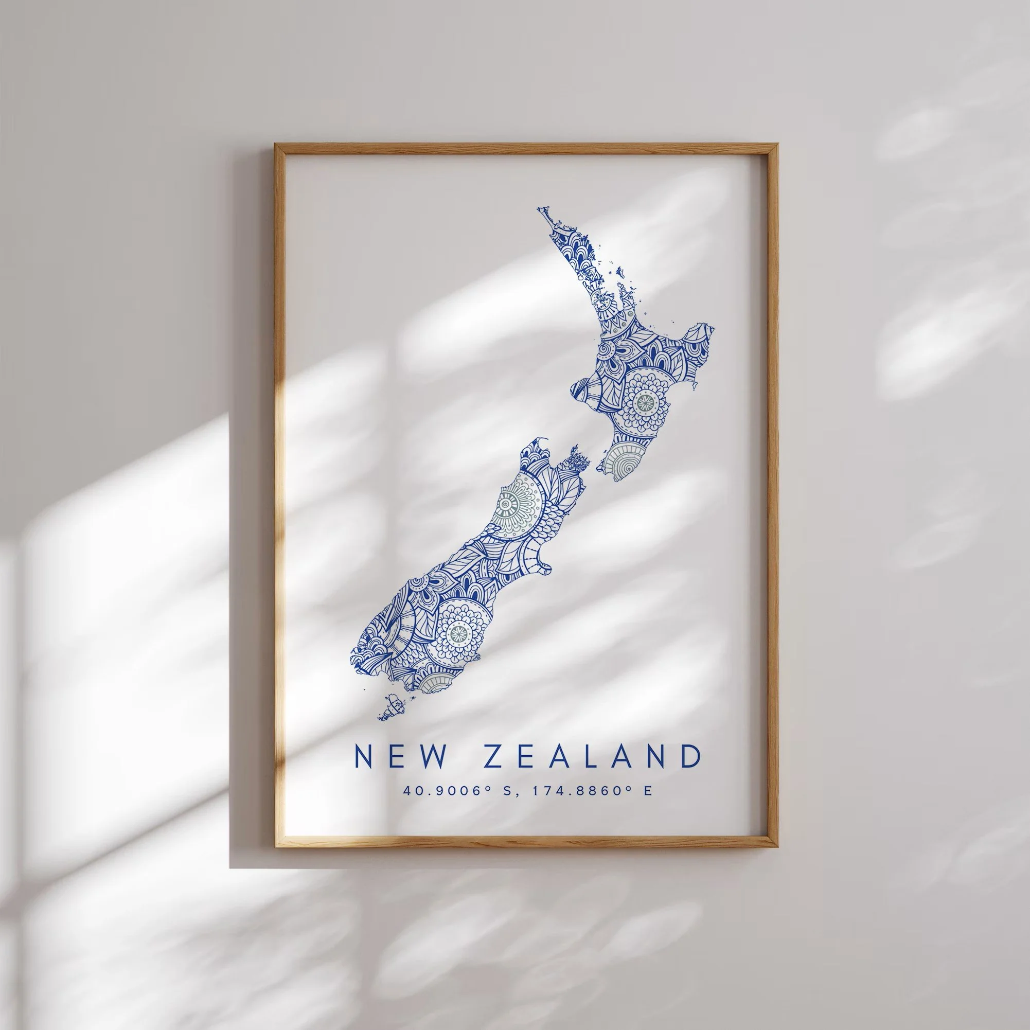 A framed map of New Zealand with a decorative blue pattern on a white background, displaying coordinates 40.9006°S, 174.8866°E, and the text 'New Zealand' underneath.