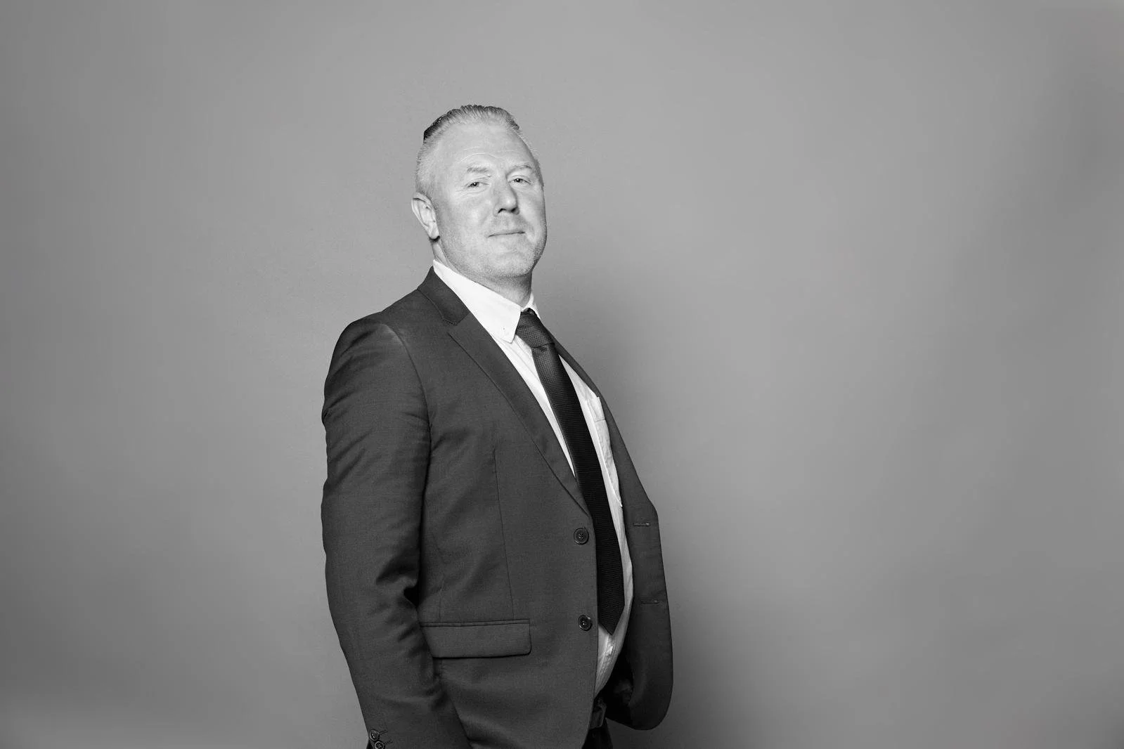 Black and white photo of a man in a suit and tie standing against a plain background.