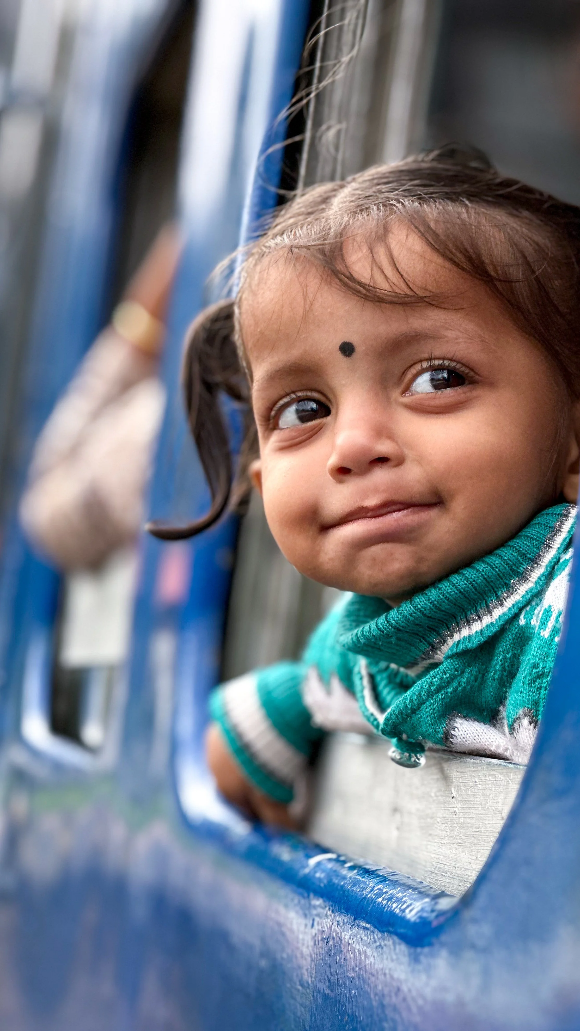 Child with a bindi looking out of a blue train window in India. Photography by Thomas Dohm.