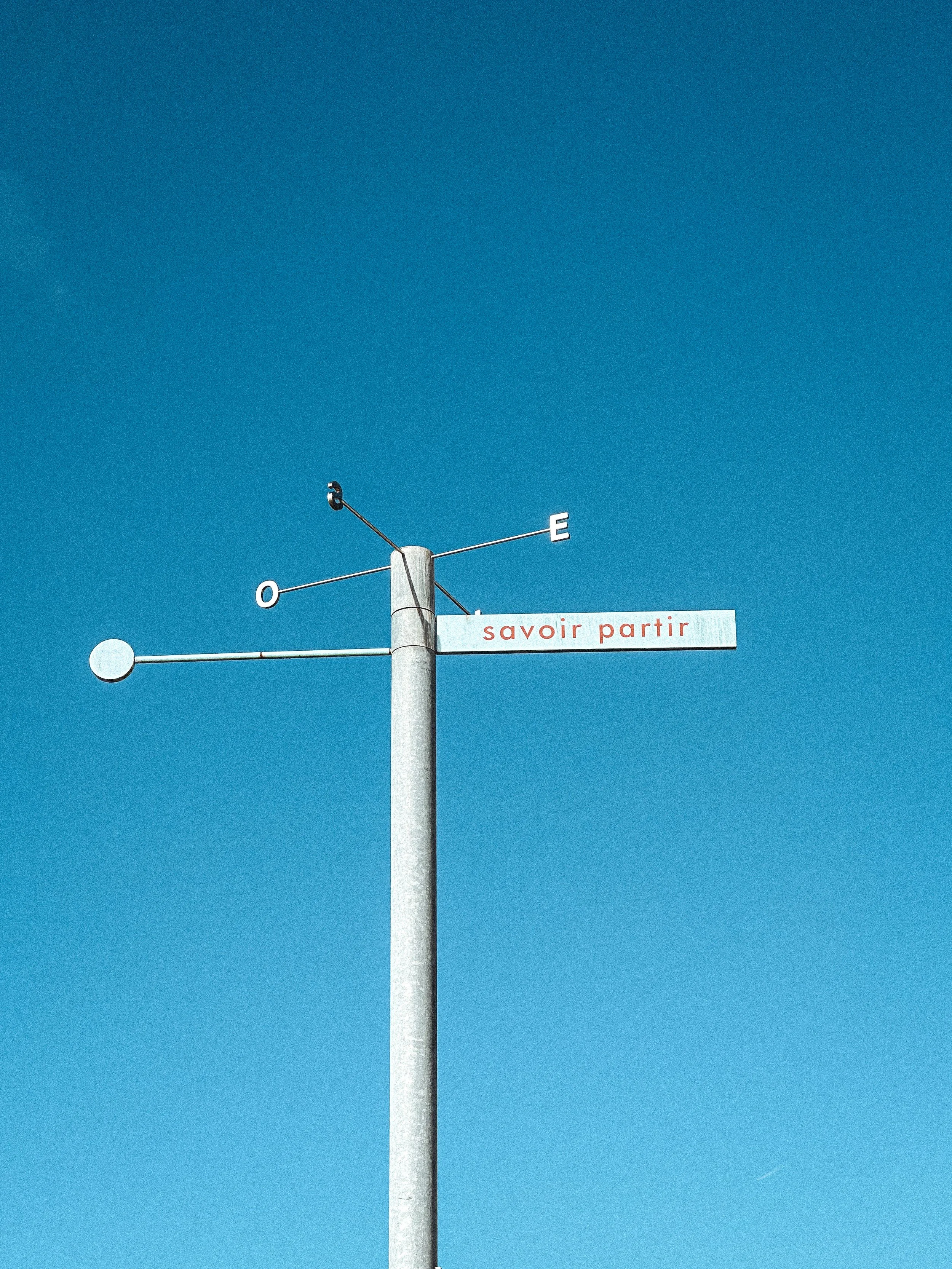 Weathervane reading "savoir partir" (knowing when to leave) against a clear blue sky in La Rochelle, France. Photography by Thomas Dohm.