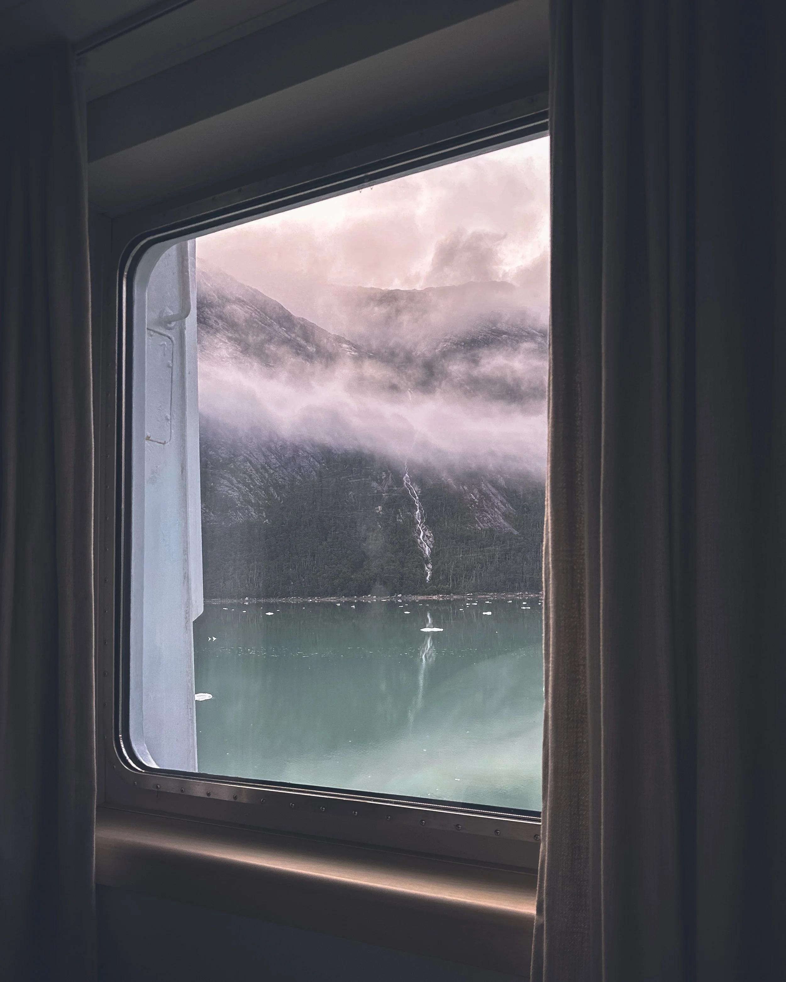 Misty glacier and still water seen through a ship cabin window in Patagonia. Photography by Thomas Dohm.