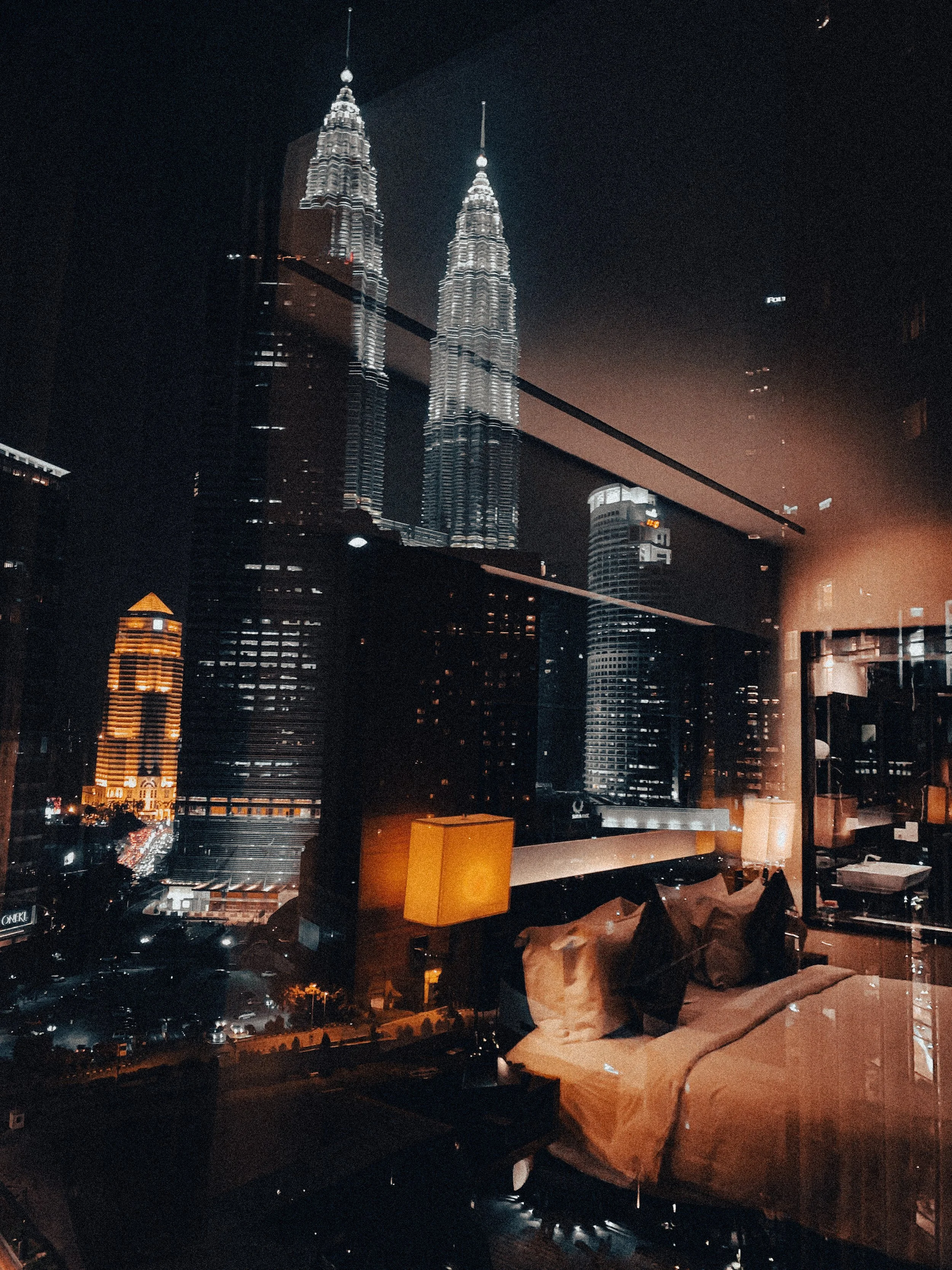 Petronas Towers at night seen through a hotel window reflection in Kuala Lumpur, Malaysia. Photography by Thomas Dohm.