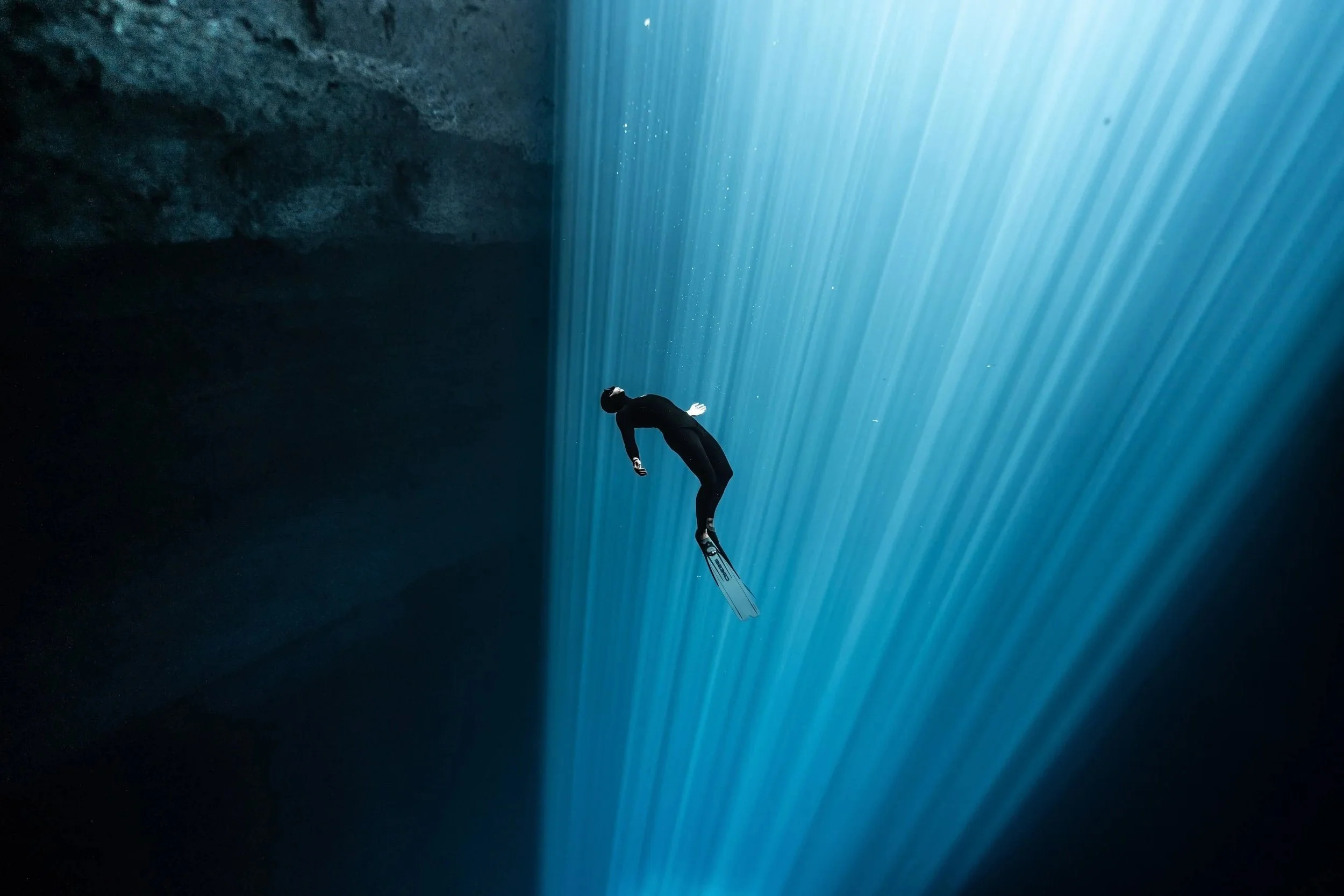 Thomas Dohm suspended in a cenote with diagonal light rays filtering through the water, Tulum, Mexico. Photographed by Matthieu Duvault.