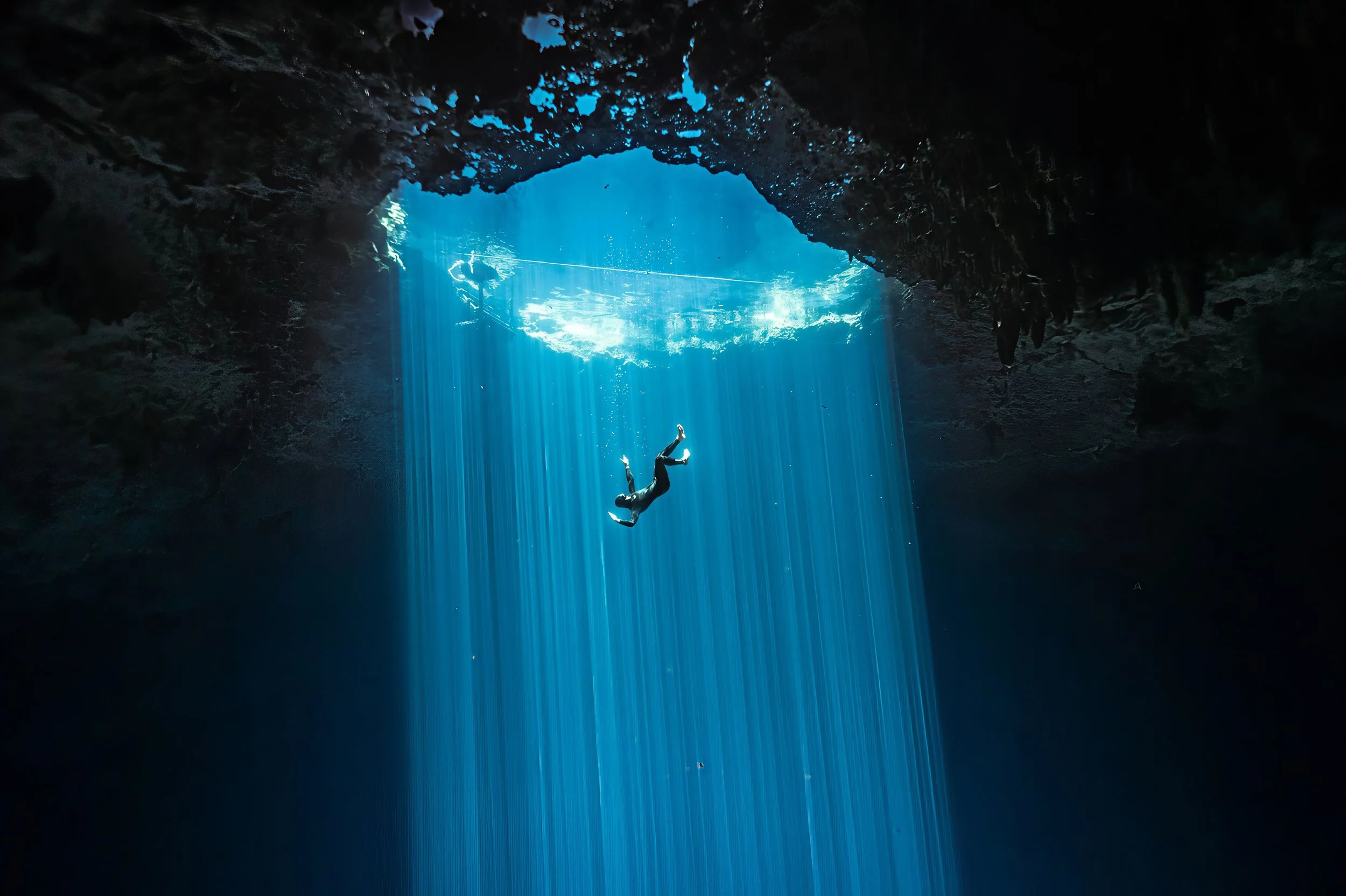 Thomas Dohm freediving through a cenote in Tulum, Mexico, descending into light rays from the surface. Photographed by Matthieu Duvault.