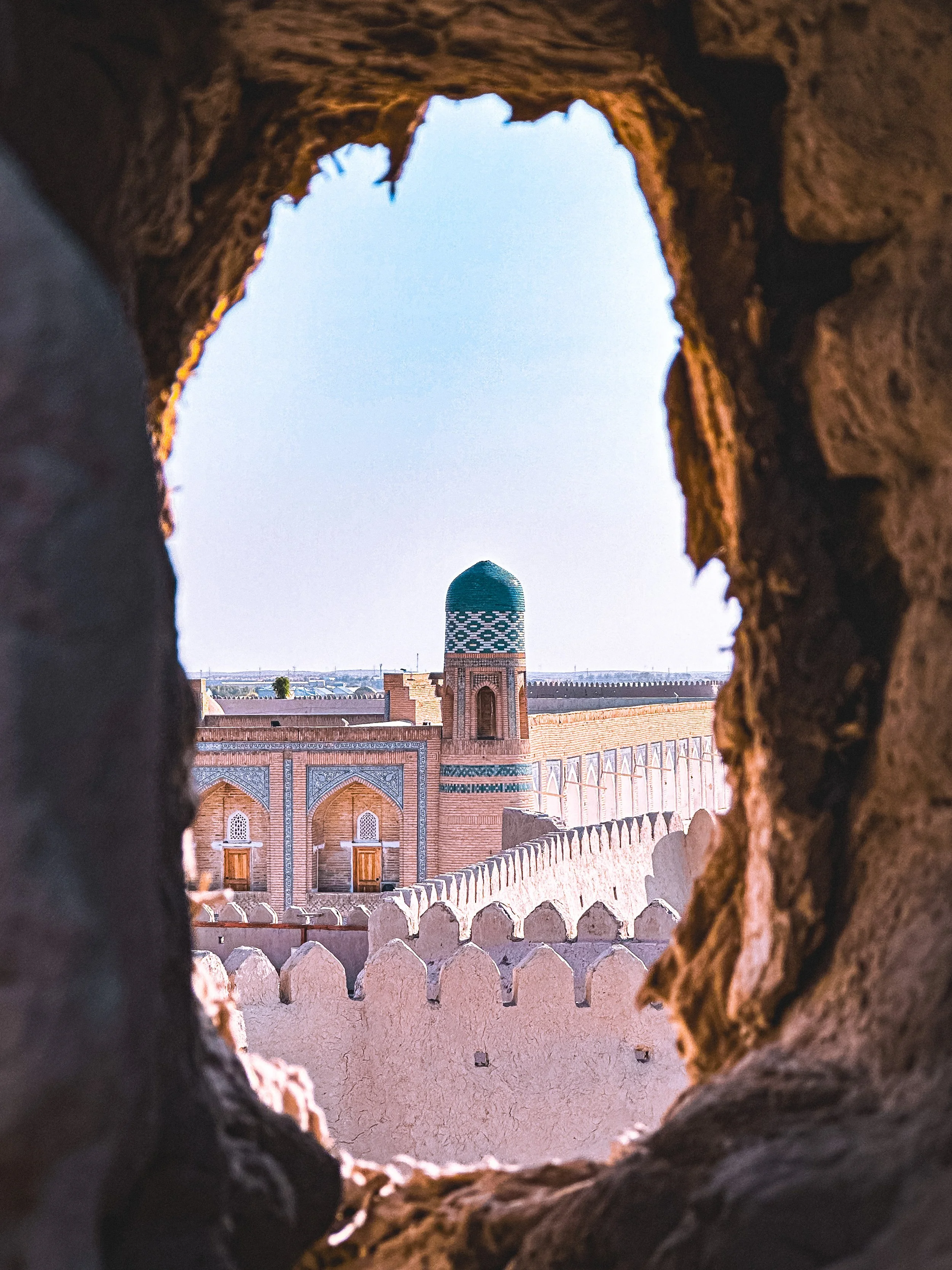 Minaret and mosque viewed through a hole in a crumbling mud wall in Khiva, Uzbekistan. Photography by Thomas Dohm.