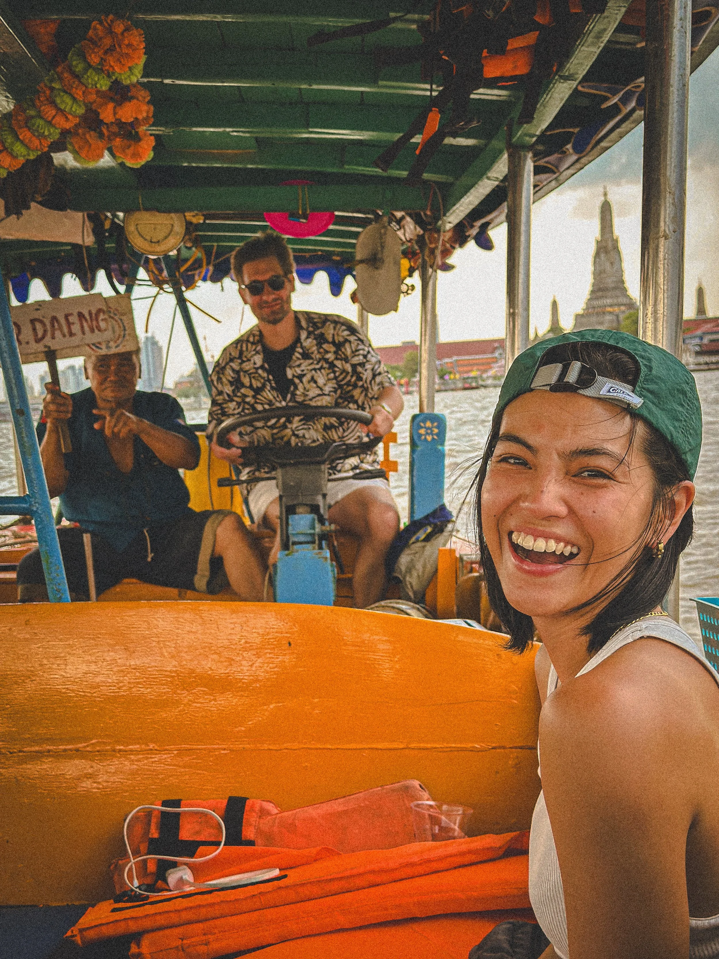 Tess laughing on a longtail boat on the Chao Phraya river in Bangkok, with Wat Arun in the background. Photography by Thomas Dohm.
