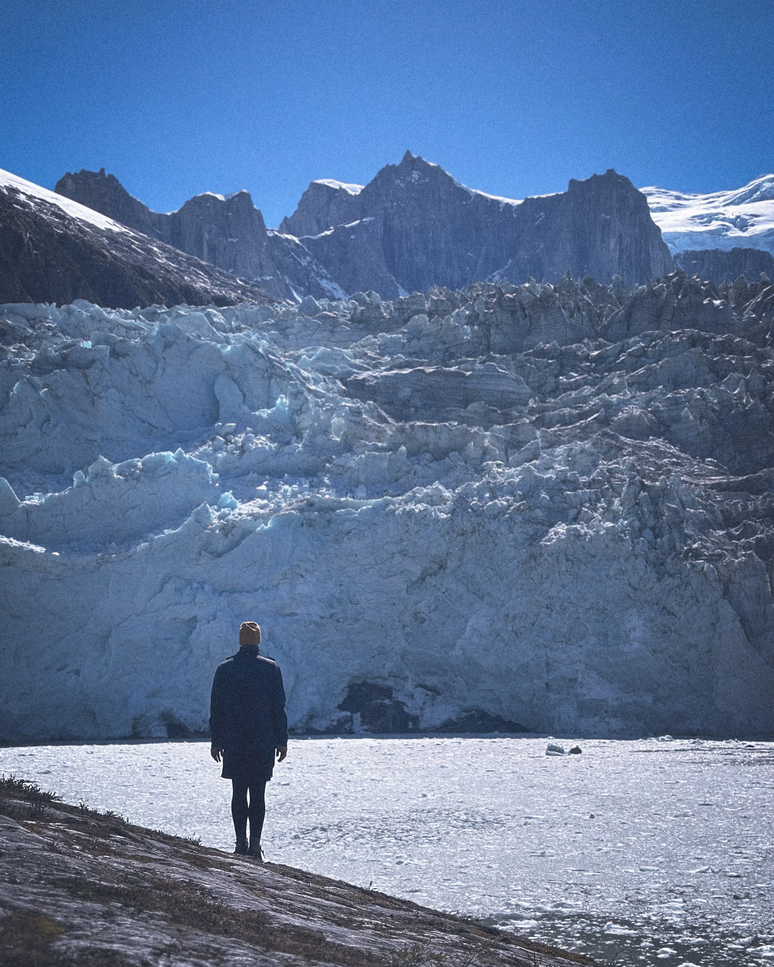 Silhouette of a figure standing before a glacier and still water in Patagonia. Photography by Thomas Dohm.
