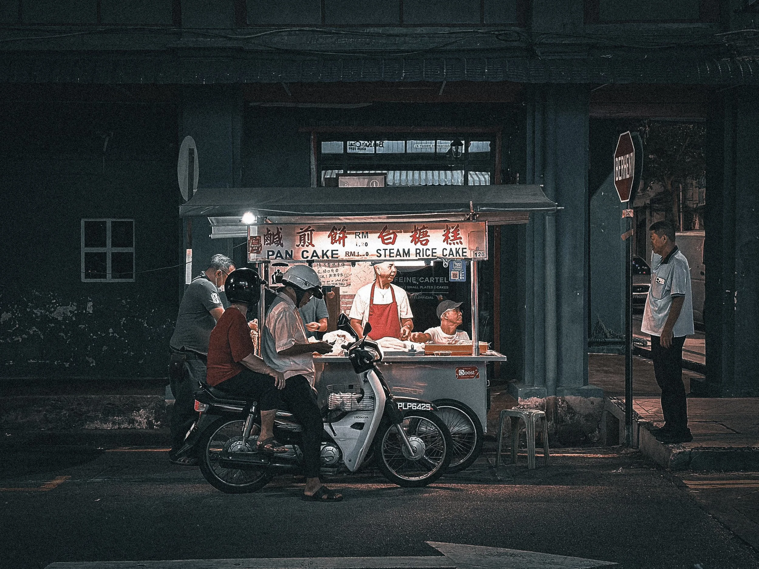 Street food stall serving steamed rice cakes at night with a motorcycle in the foreground, Penang, Malaysia. Photography by Thomas Dohm.