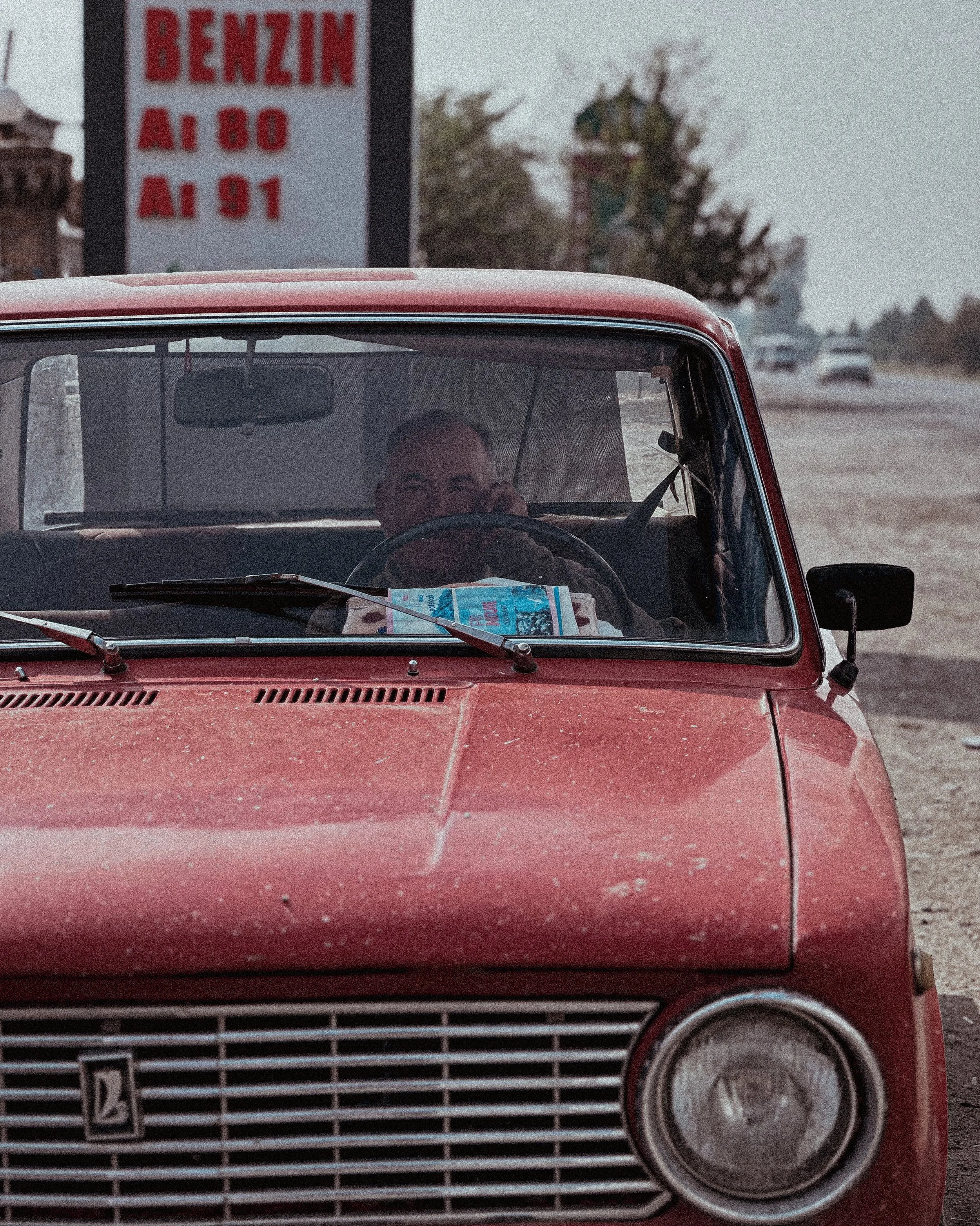 Man behind the wheel of a red Lada at a petrol station in Turkmenistan. Photography by Thomas Dohm.