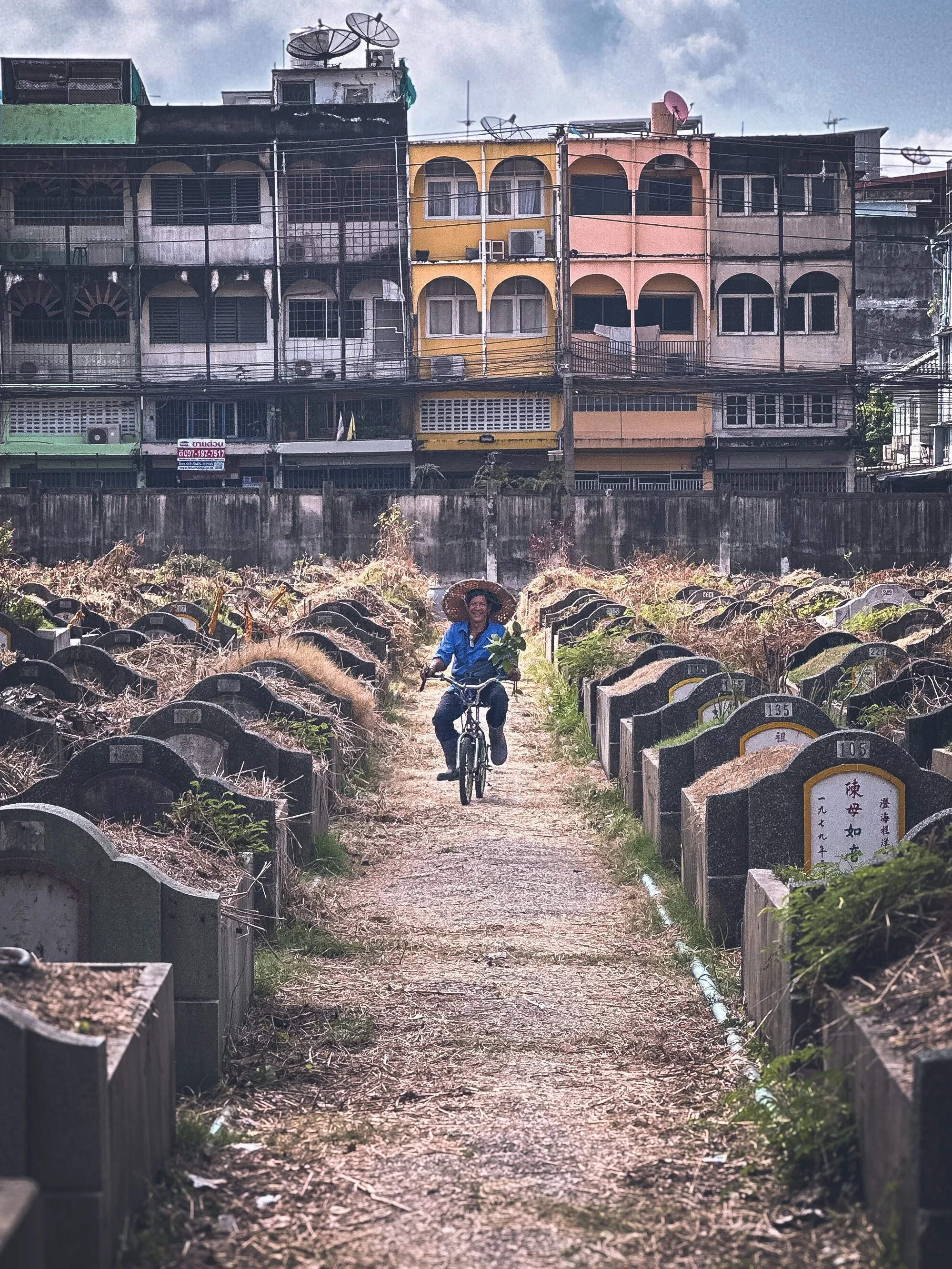 Cyclist riding through the Teochew Cemetery Parl with colourful shophouses above in Bangkok, Thailand. Photography by Thomas Dohm.