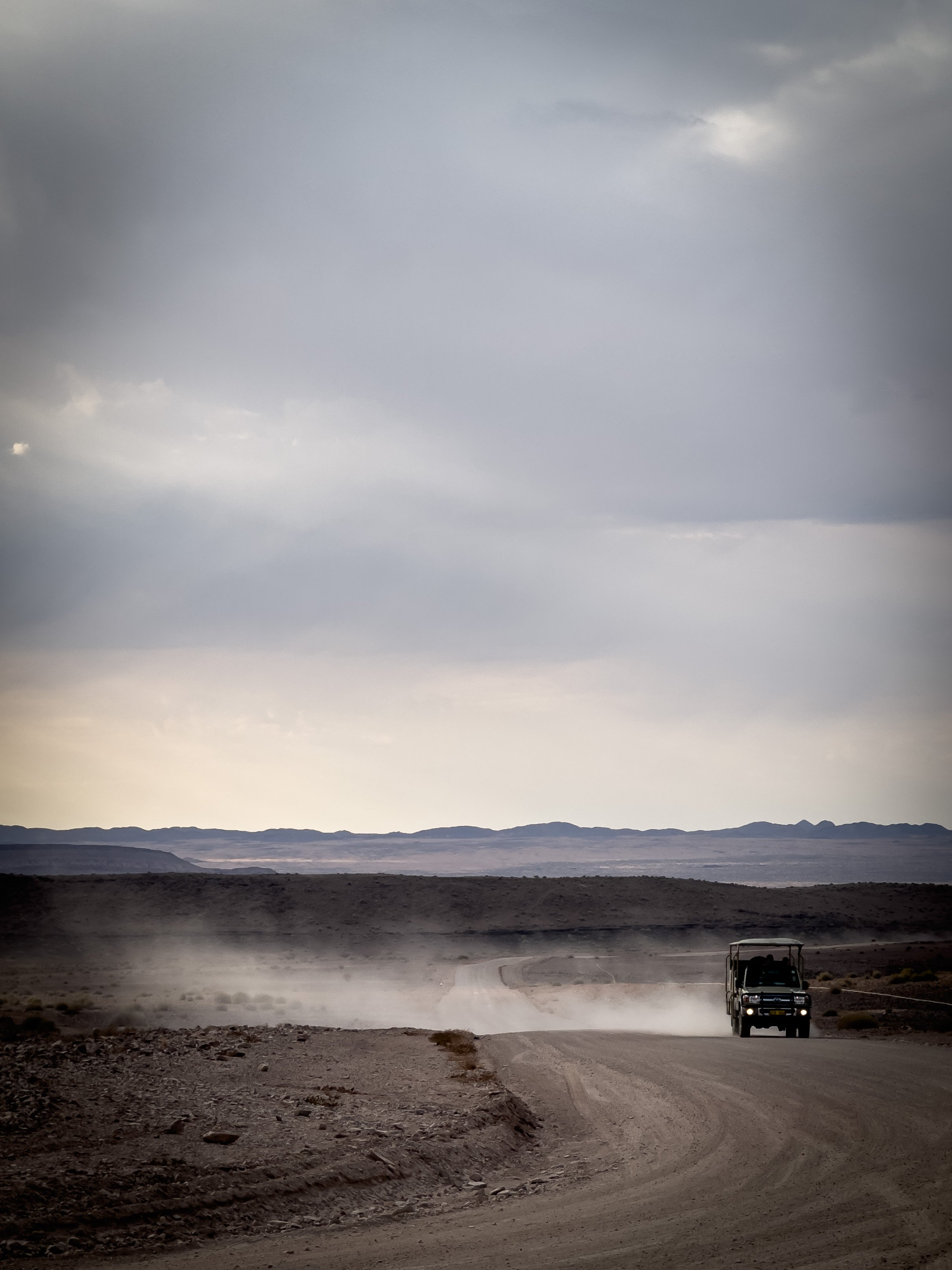 Vehicle trailing dust on a desert road across the Namib Desert, Namibia. Photography by Thomas Dohm.