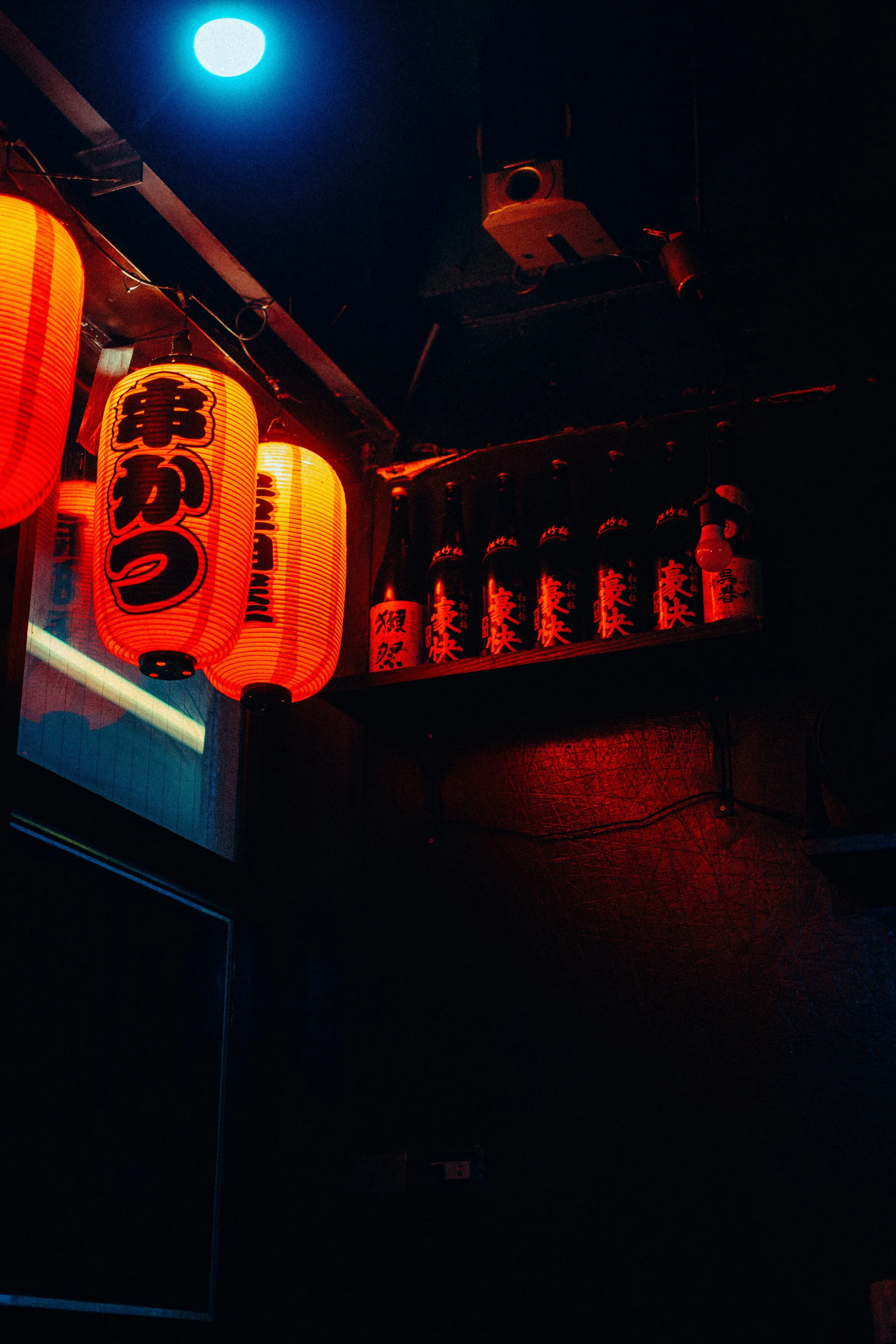 Red Japanese paper lanterns with black characters hanging in a dimly lit space, under a bright full moon