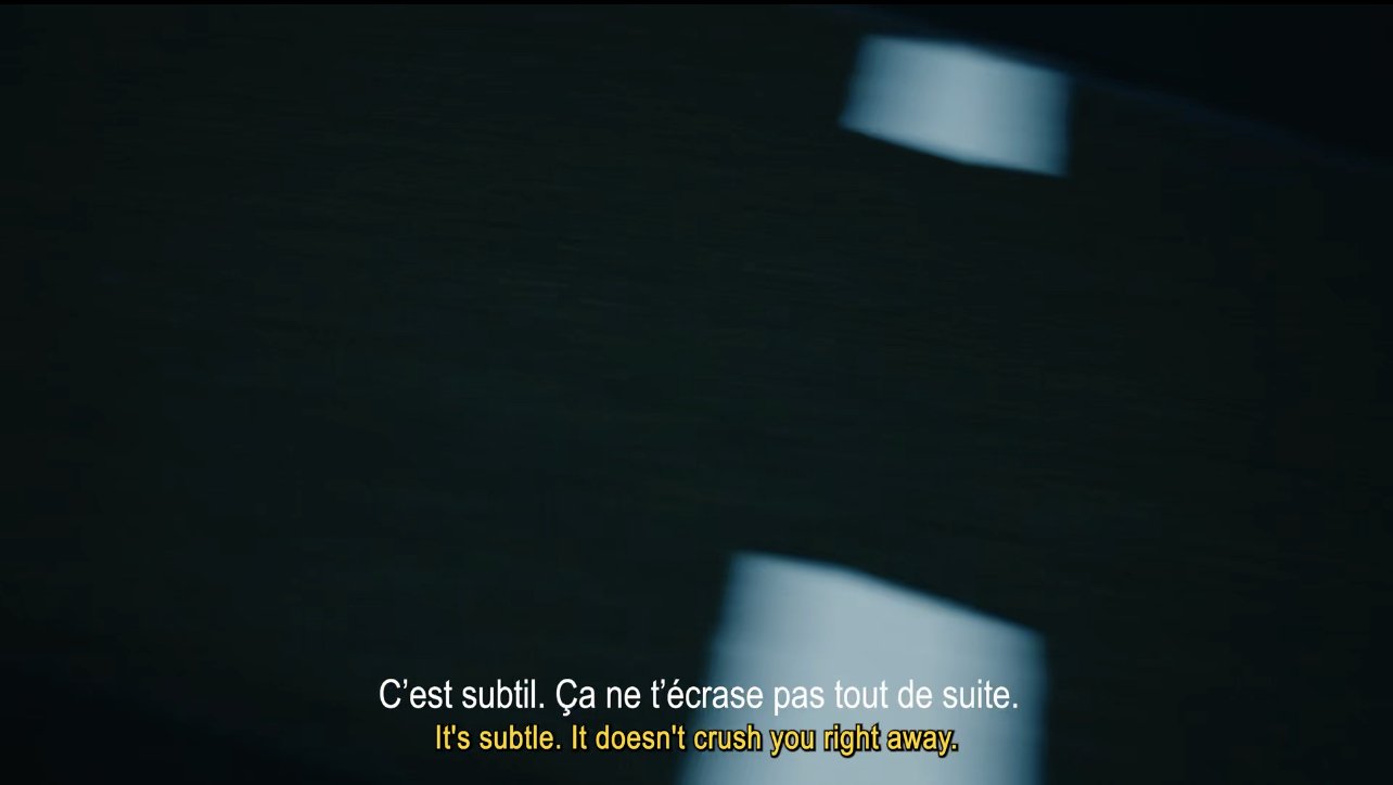 Dark background with two light reflections and French and English subtitles reading: "It's subtle. It doesn't crush you right away."