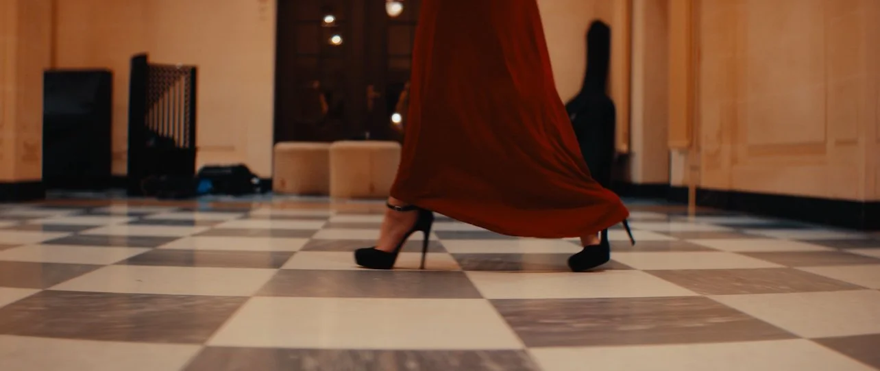 Person dancing in a red dress and black high heels on a checkered floor.