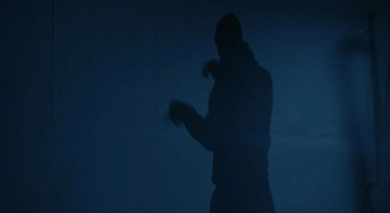 Silhouette of a person standing in a dimly lit, dark blue space.
