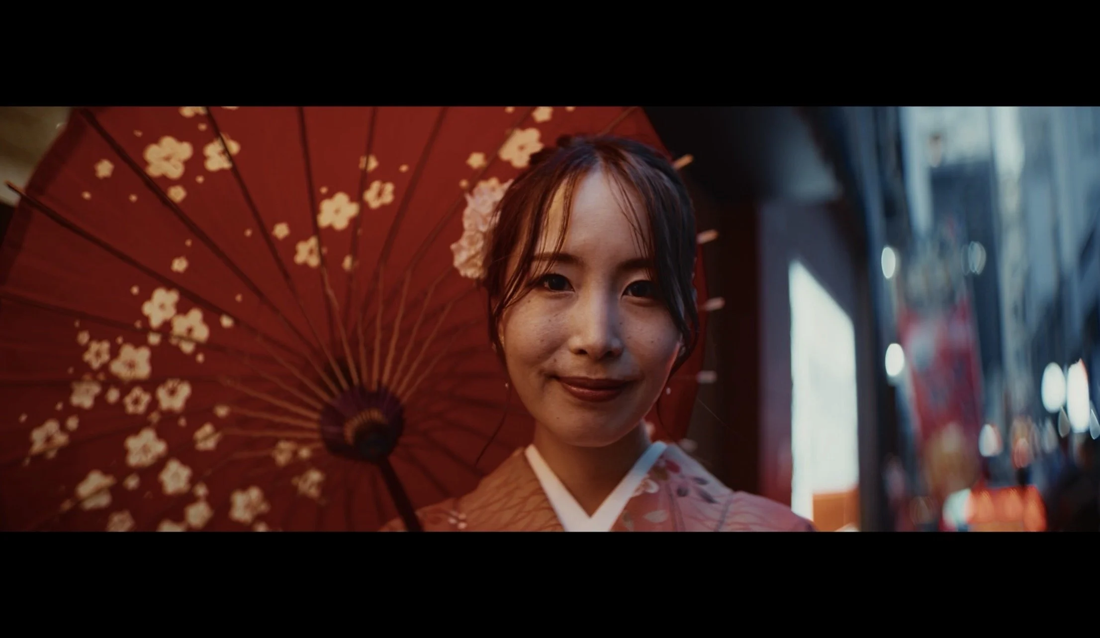 A young woman in traditional Japanese attire holding a red umbrella with white floral patterns.