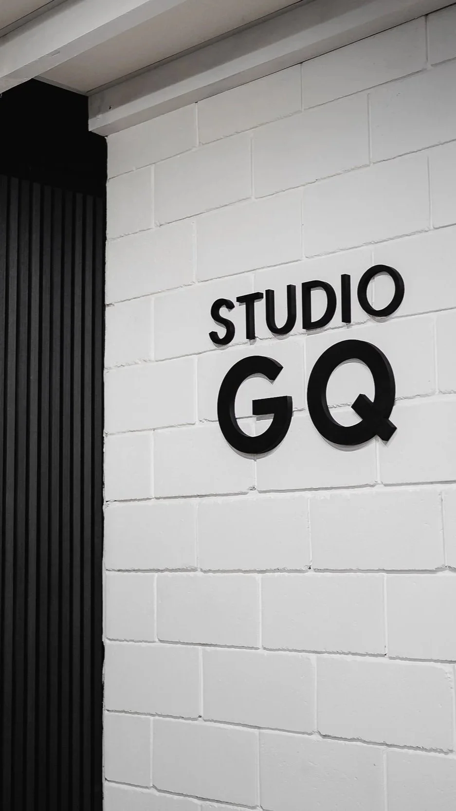 Sign on a white brick wall that reads 'STUDIO GQ' in black letters.