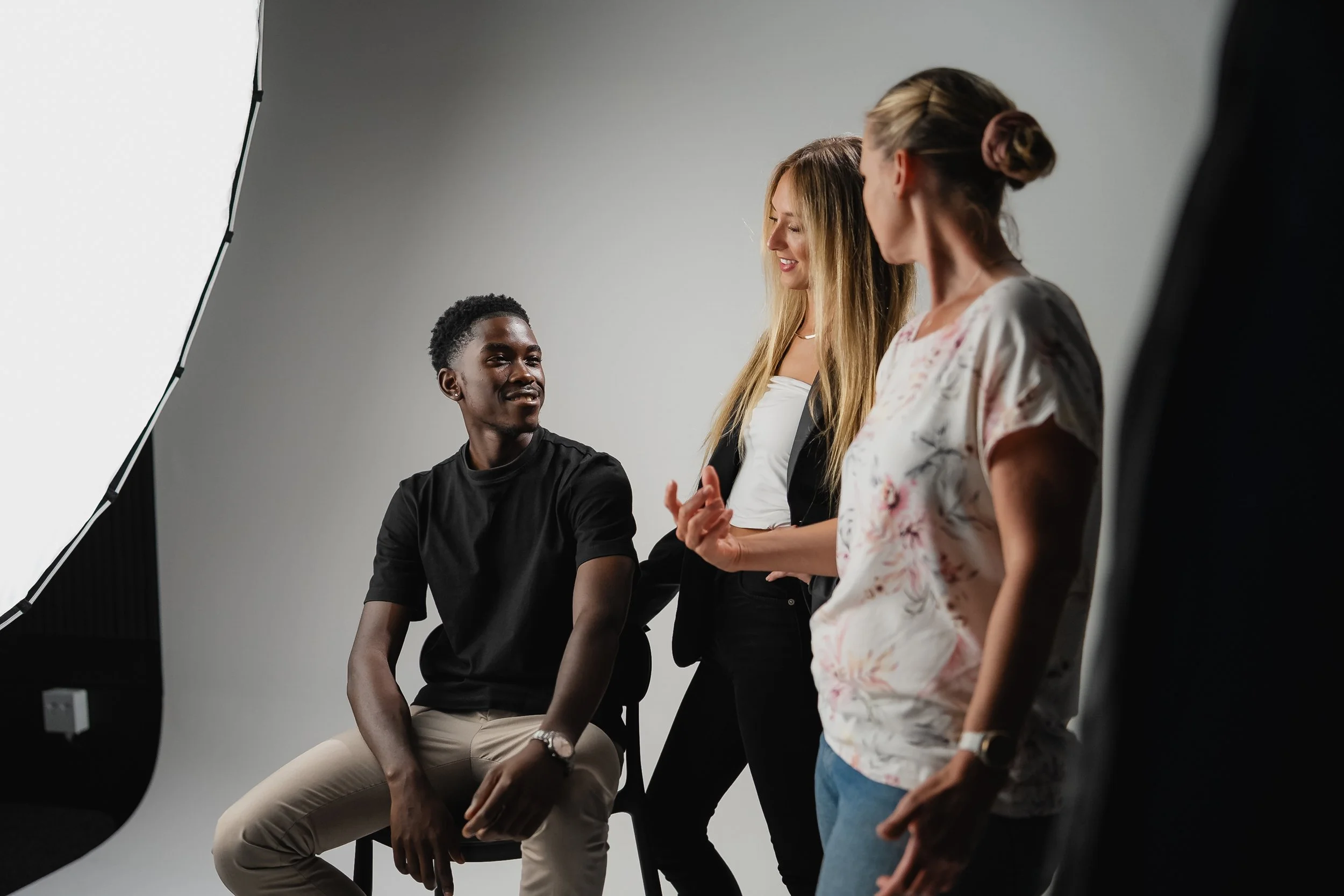 People in a photography studio doing a photo shoot, with a large light diffuser on the left and a gray backdrop.