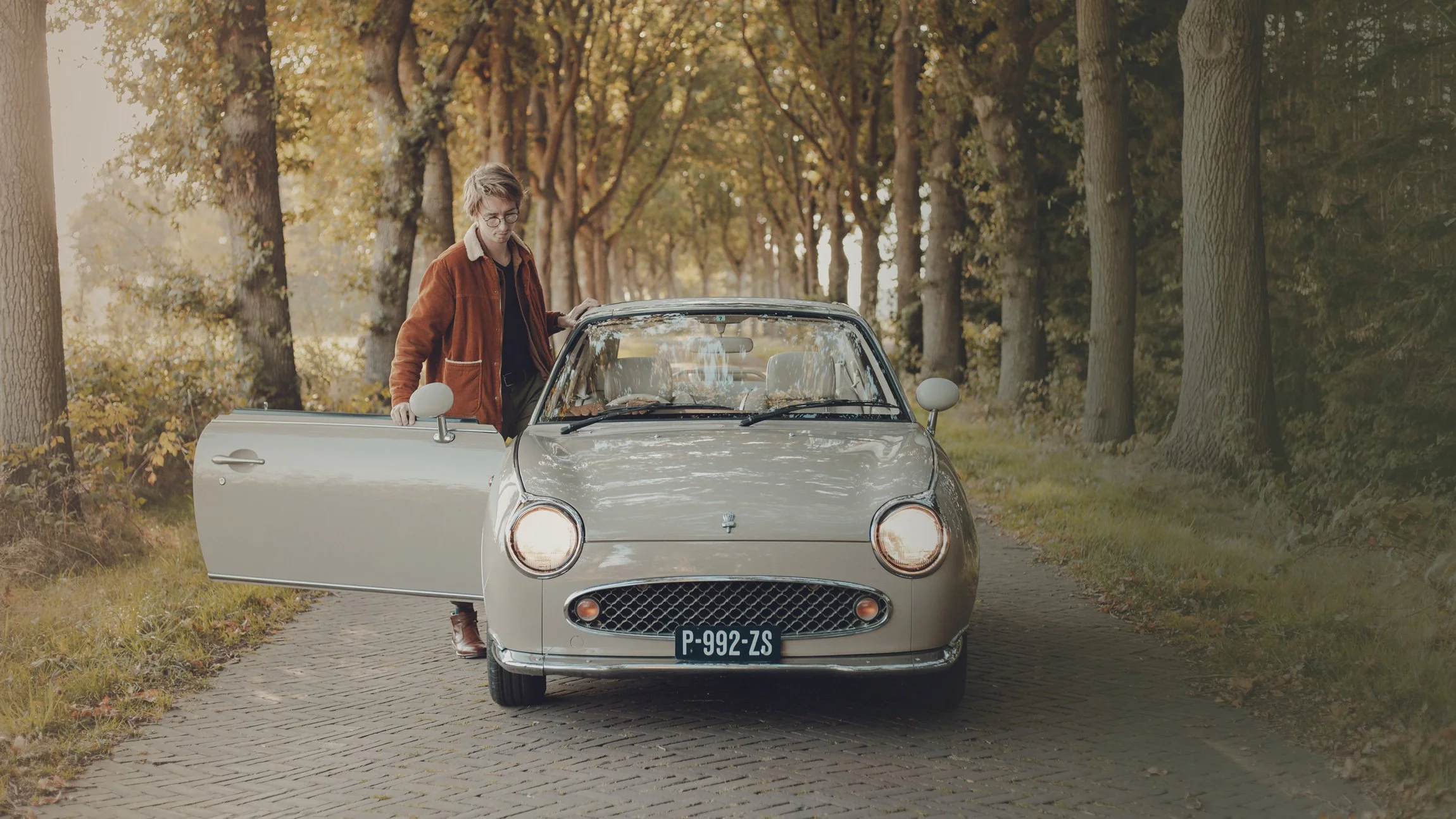 Persoon stapt uit auto op landelijke weg omringd door bomen in warme herfstsfeer