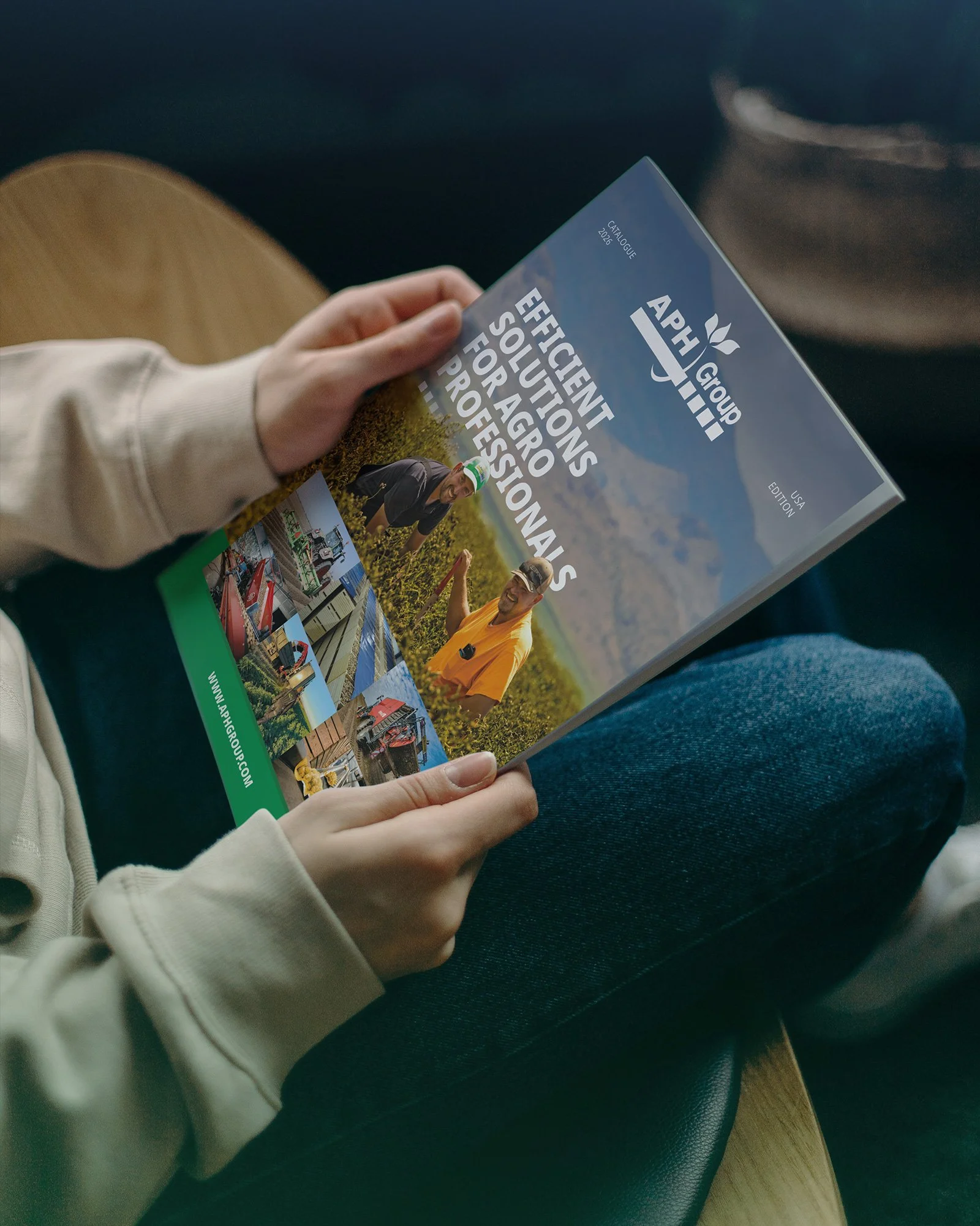 A person holding a brochure titled 'Effective Solutions for Aggro Professionals' by APH Group, featuring images of farm machinery and workers, with a field and mountains in the background.