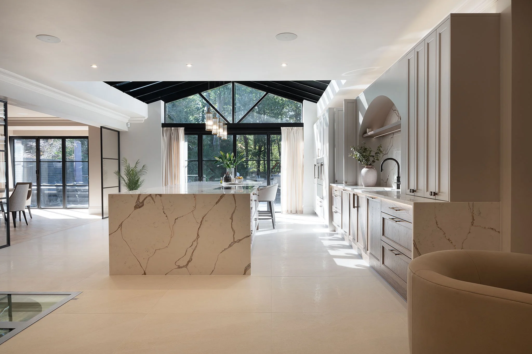 Modern kitchen with white cabinets, marble island, large windows, and black ceiling with pendant lights.