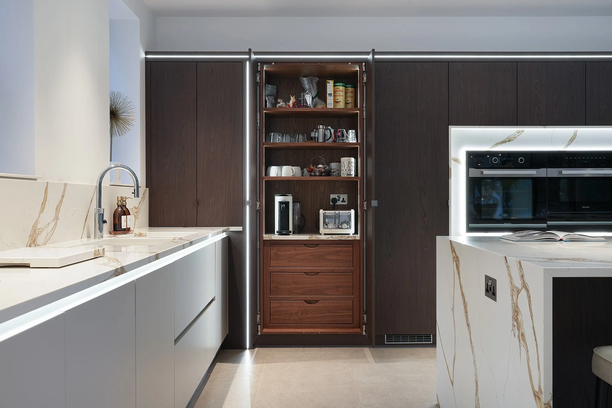Modern kitchen with white and dark wood cabinetry, marble countertops, and open shelves with kitchenware.