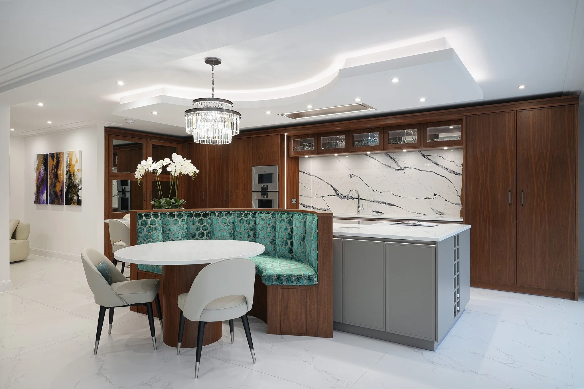 Modern kitchen with white marble backsplash, wooden cabinets, and a gray kitchen island. Includes a dining area with a round table and mixed chairs, chandelier, and decorative artwork on the wall.