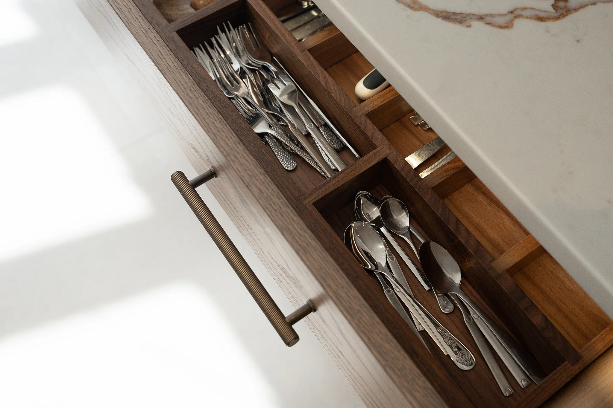 Open kitchen drawer with silverware organized in sections, including forks, spoons, and knives.