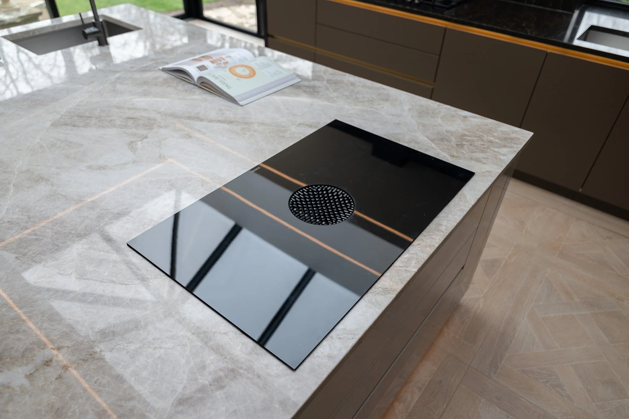Modern kitchen island with a built-in black induction cooktop and a magazine on a marble countertop.